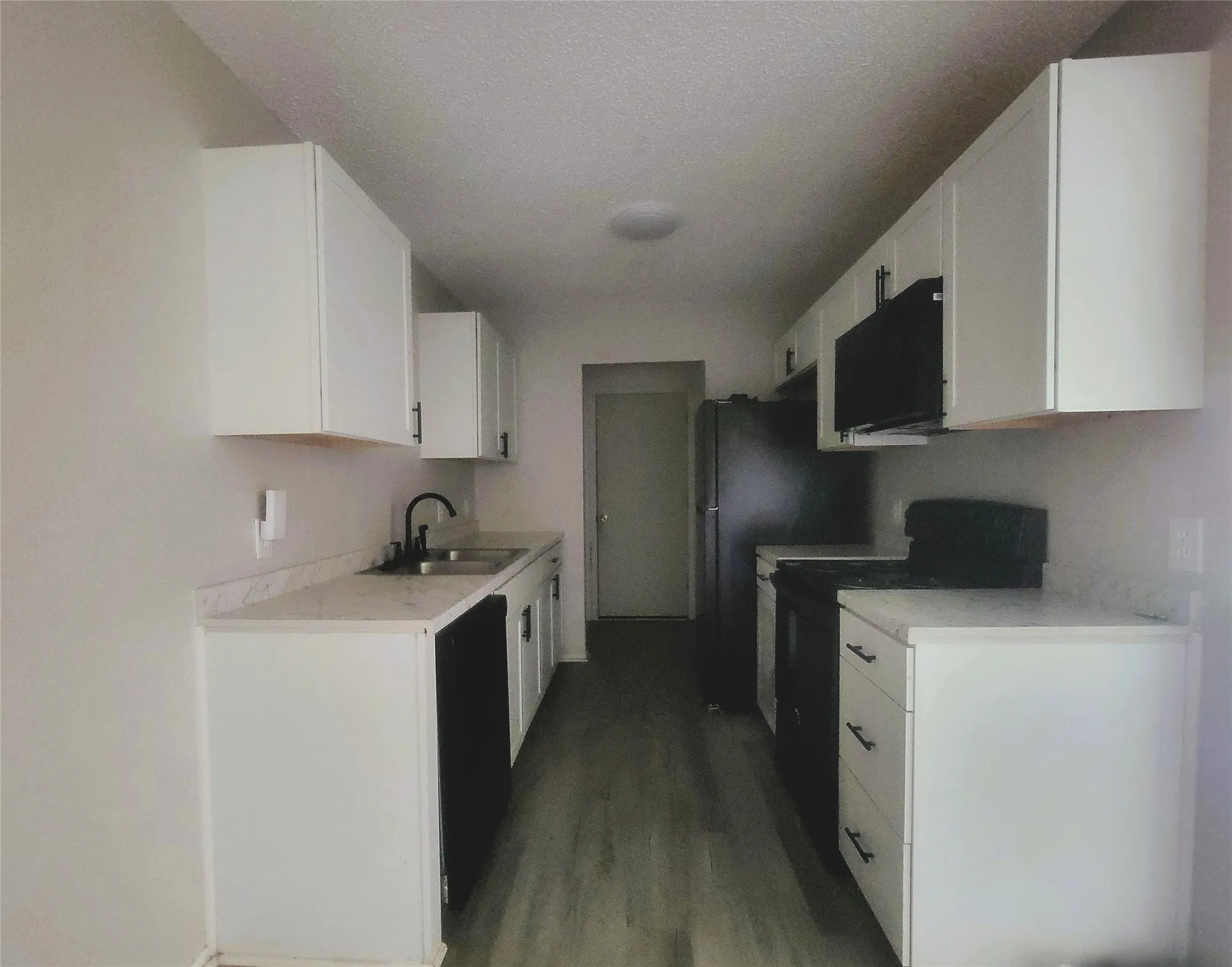 Galley kitchen featuring white cabinetry, light countertops, matte black appliances, a double basin sink with a gooseneck faucet, and wood-finish flooring