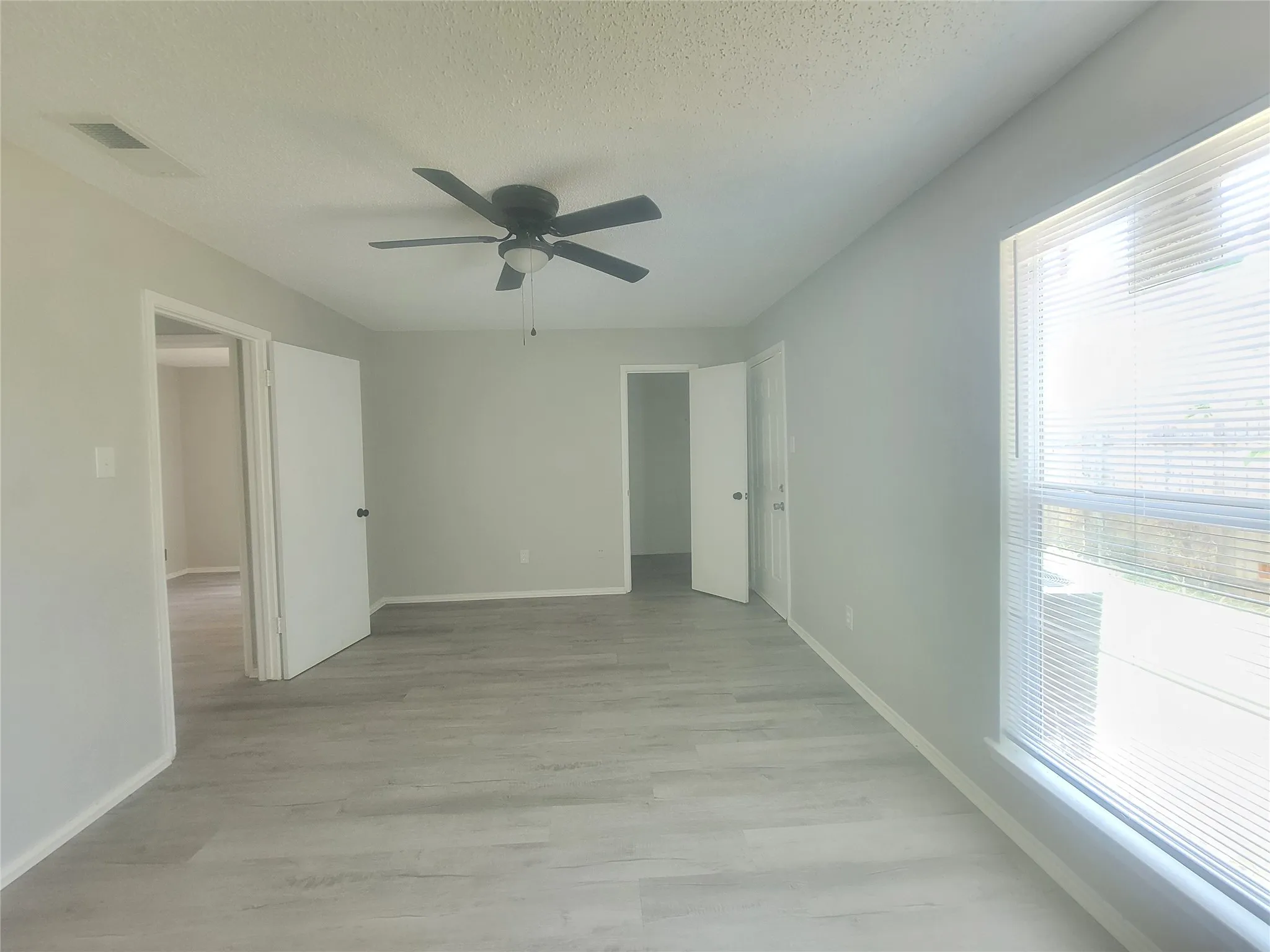 Spacious interior room featuring light gray walls, wood-finish flooring, and a ceiling fan with integrated lighting