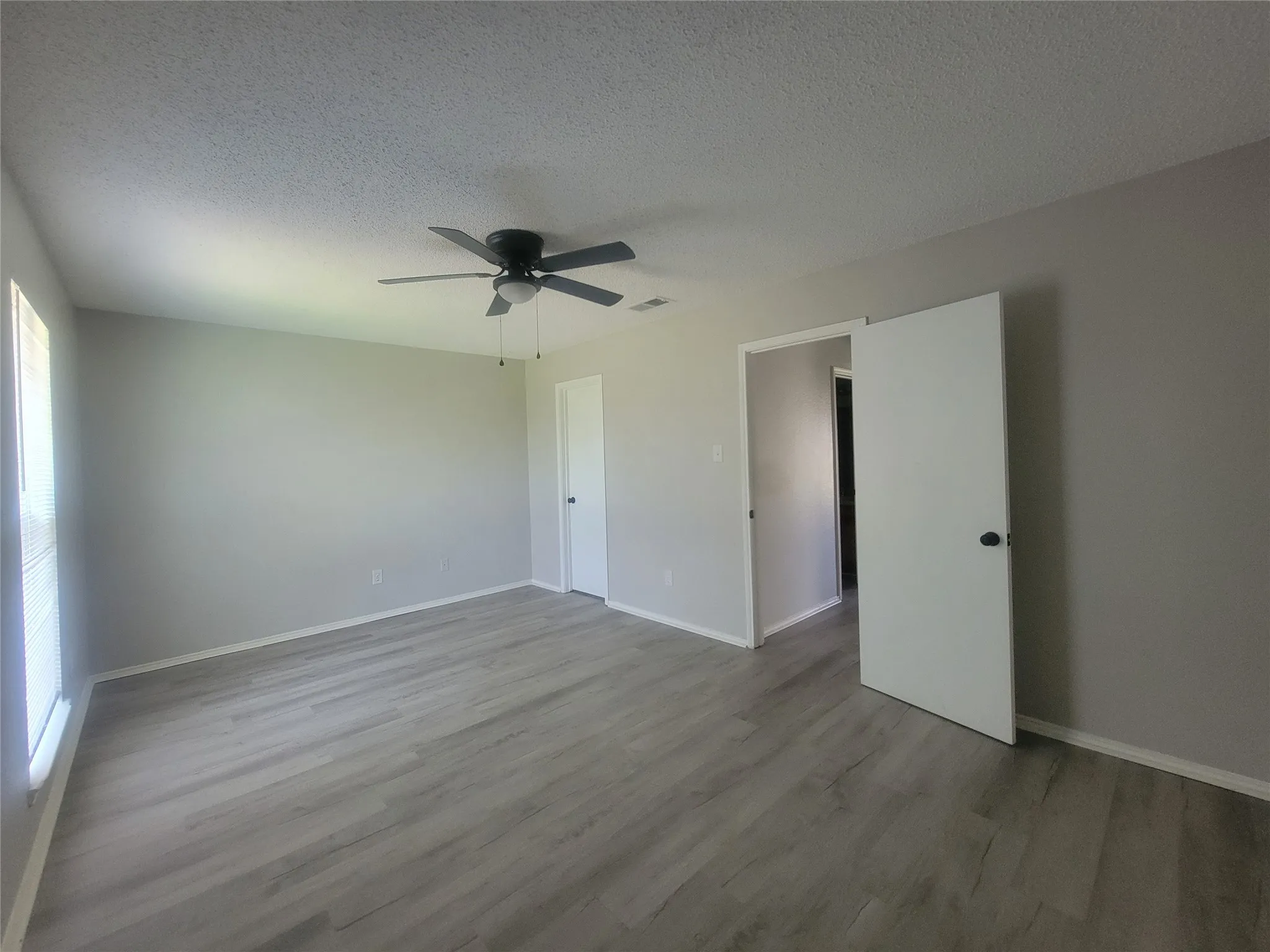 Spacious room featuring light gray walls, wood-finish flooring, a ceiling fan with integrated lighting, and multiple doorways