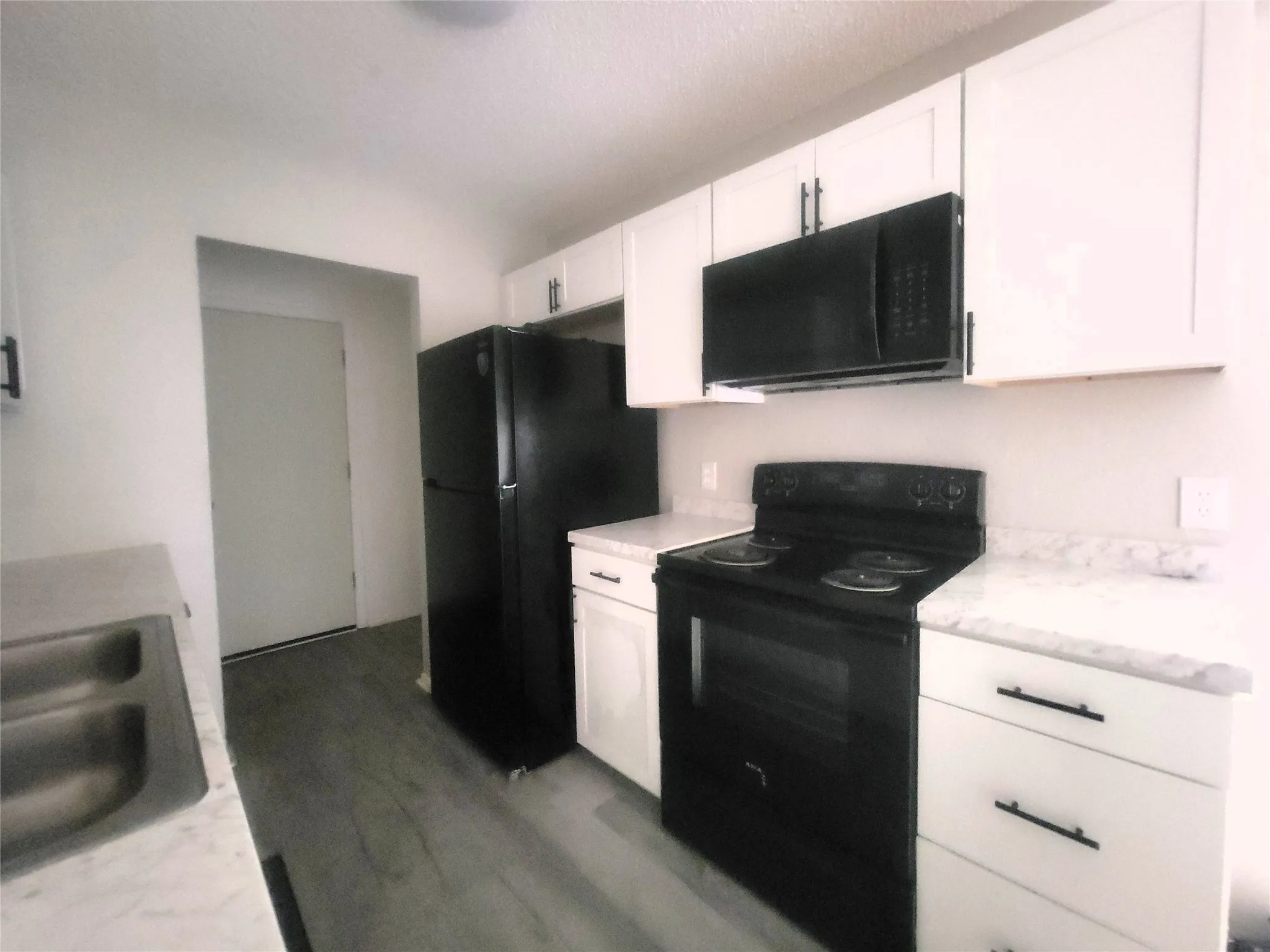 Modern kitchen featuring white cabinetry with integrated hardware, black stainless steel appliances including a range and refrigerator, quartz countertops, and a stainless steel microwave mounted above the range