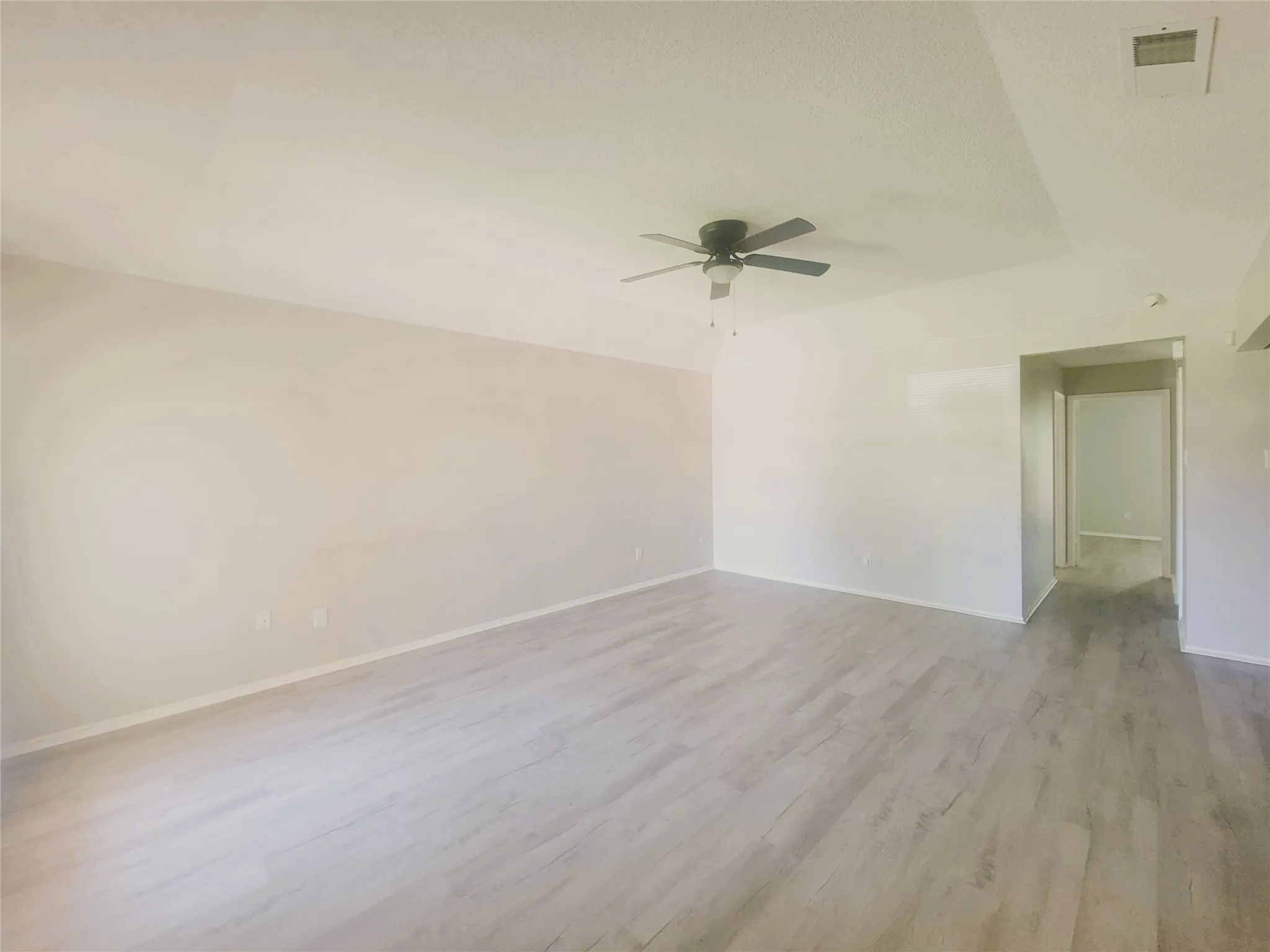 Spacious interior featuring light wood-finish flooring, neutral wall tones, and a ceiling fan with integrated lighting