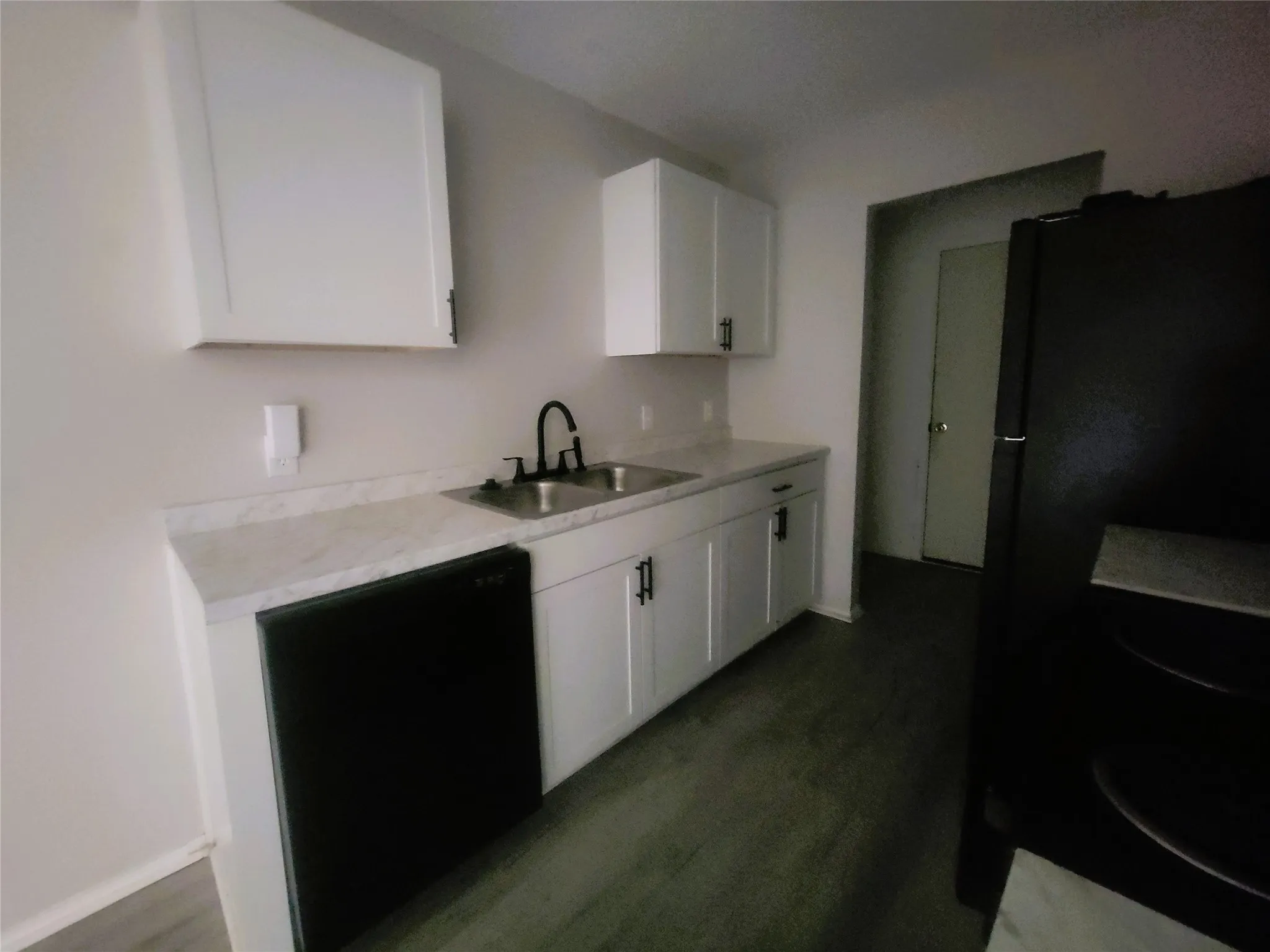Kitchen featuring white shaker-style cabinetry, light-toned countertops, a black double-basin sink with a matte black faucet, a black dishwasher, and wood-finish flooring