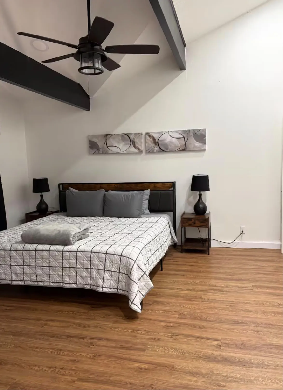 Vaulted ceiling bedroom featuring wood-finish flooring, exposed ceiling beams, and a modern ceiling fan with integrated lighting