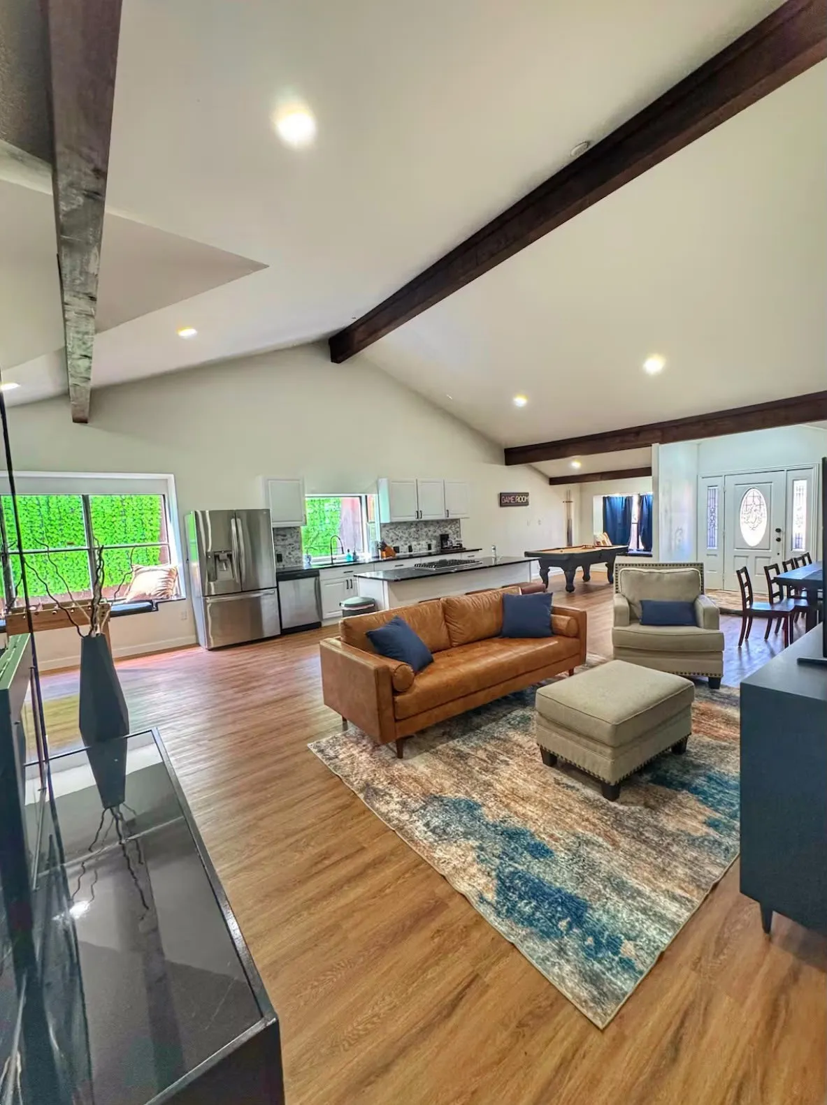 Expansive open-concept living space featuring vaulted ceilings with exposed wood beams, recessed lighting, and wood-finish flooring
