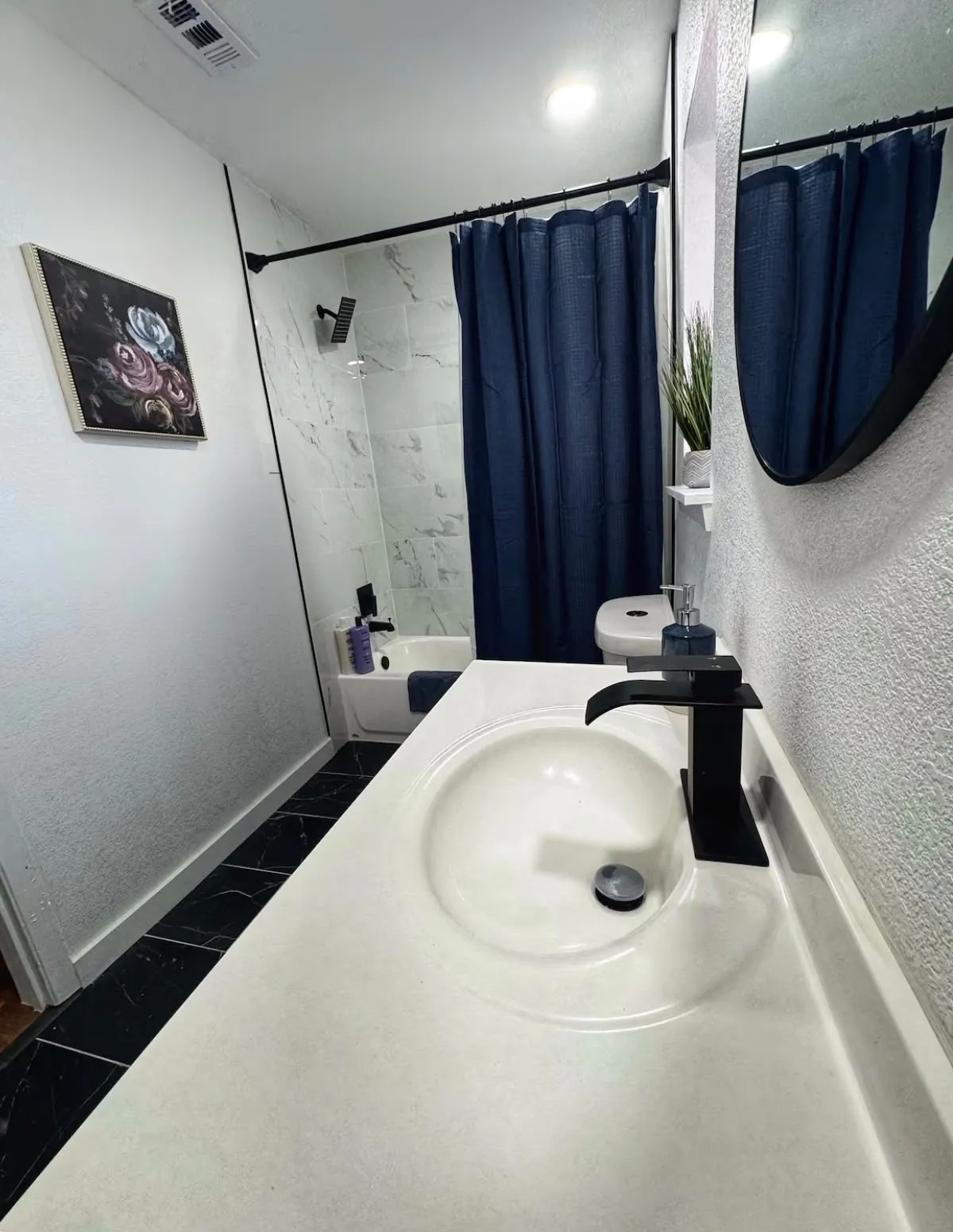 Bathroom featuring a built-in vanity with an integrated sink, matte black faucet, and a black-framed oval mirror