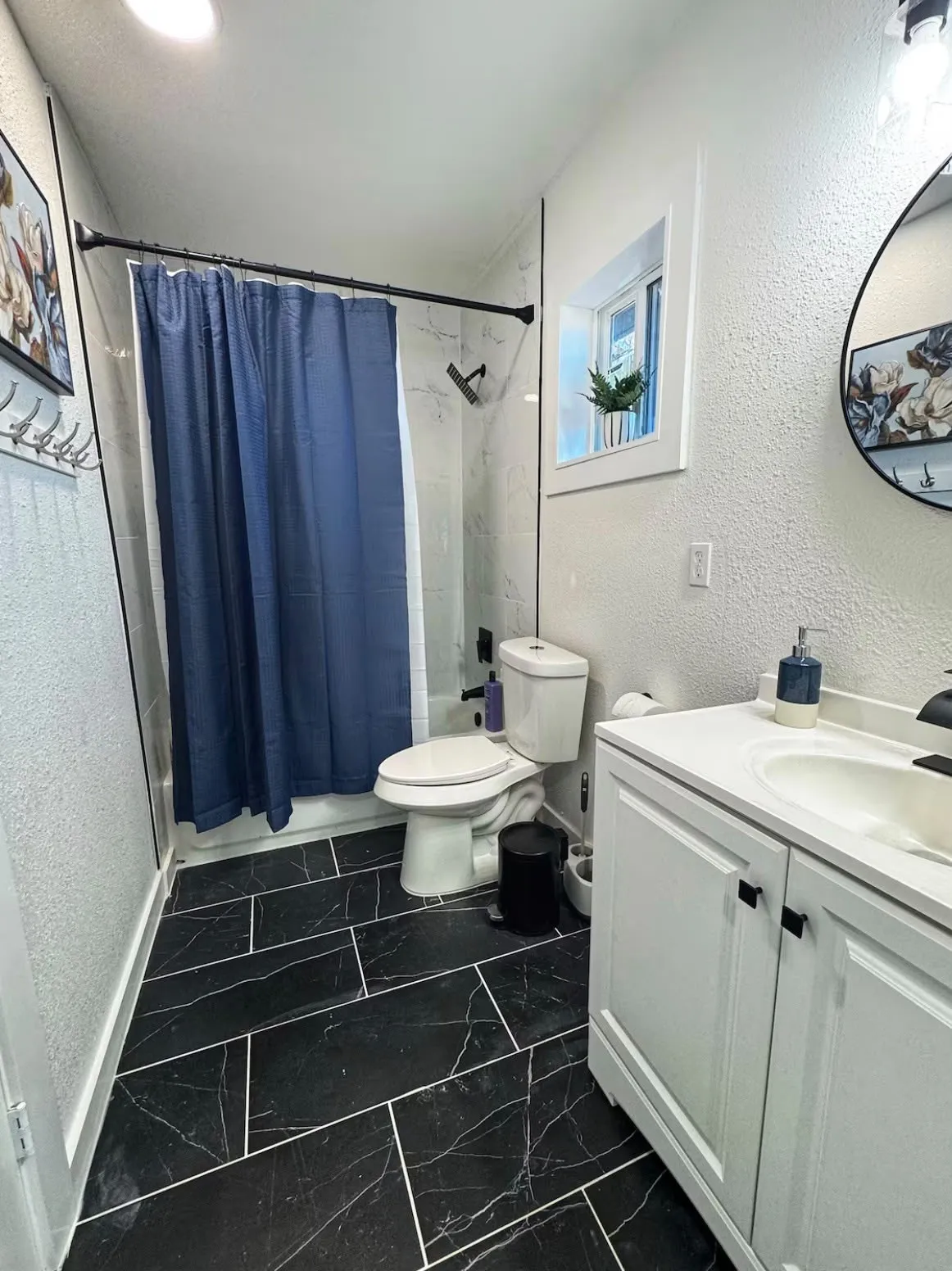 Bathroom featuring black marble-look tile flooring with white grout, a white vanity with an integrated sink, and white textured walls