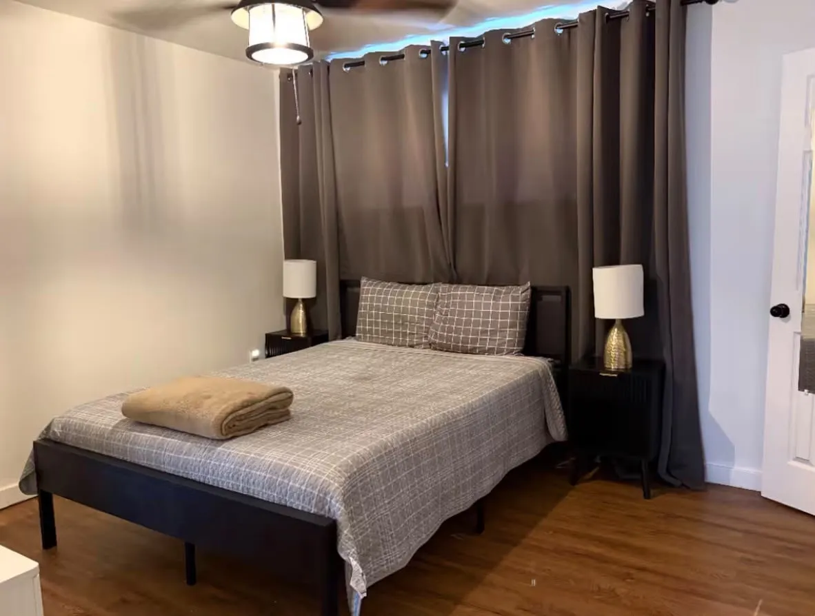 Bedroom featuring wood-finish flooring, a ceiling fan with integrated lighting, and dark window treatments