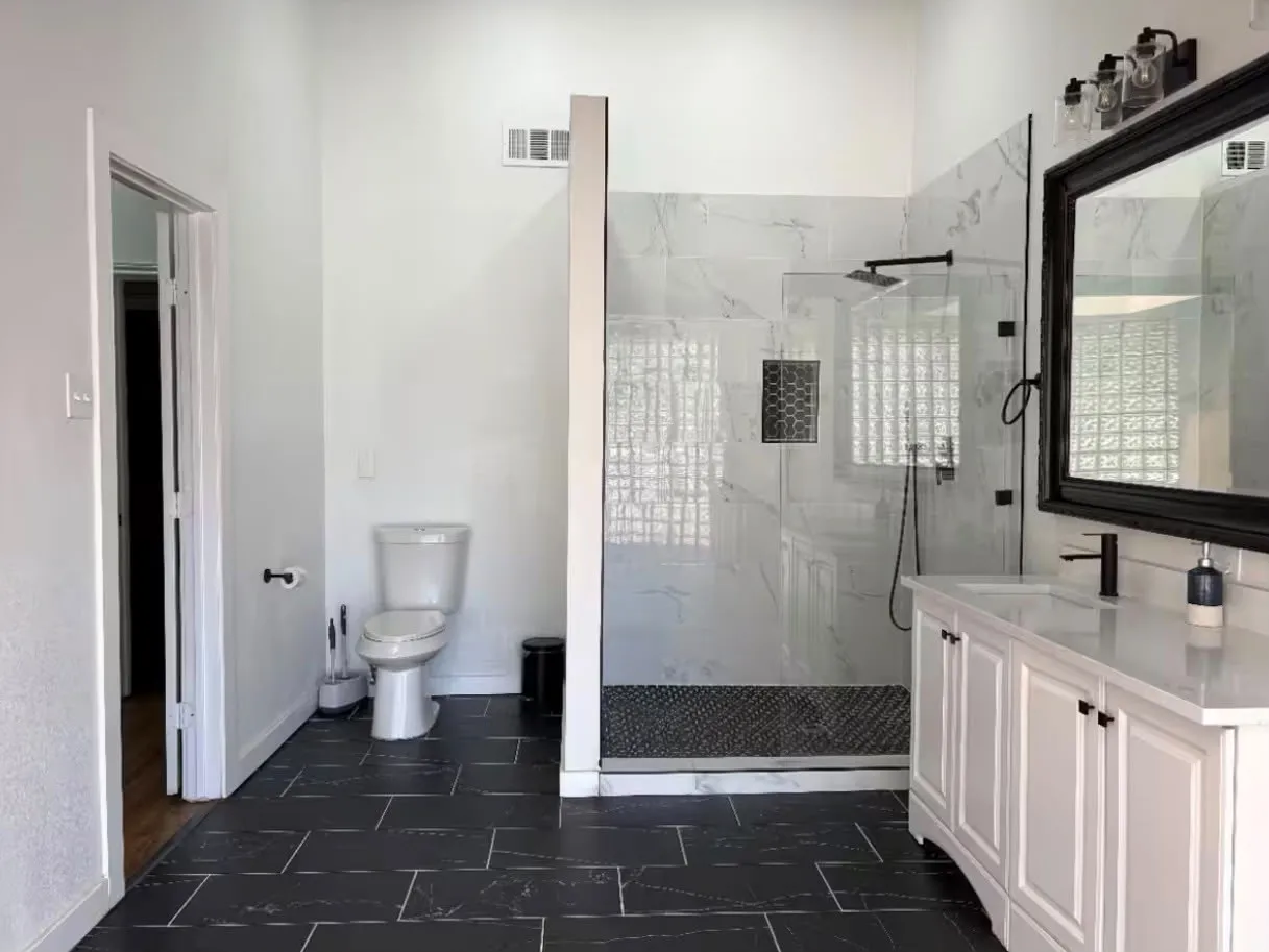 Contemporary bathroom featuring a spacious glass-enclosed shower, white marble-look wall tiling, and black-finish hardware