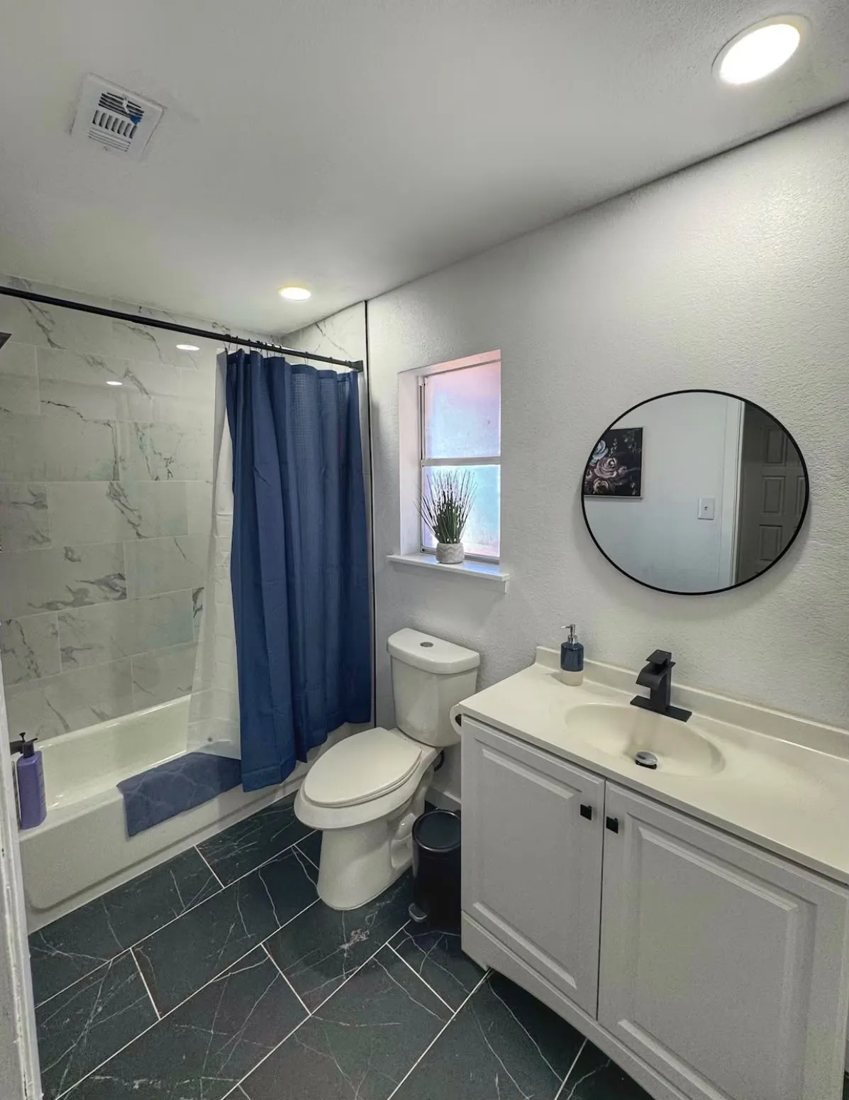 Bathroom featuring a white vanity with integrated sink, black matte faucet, and a round black-framed mirror