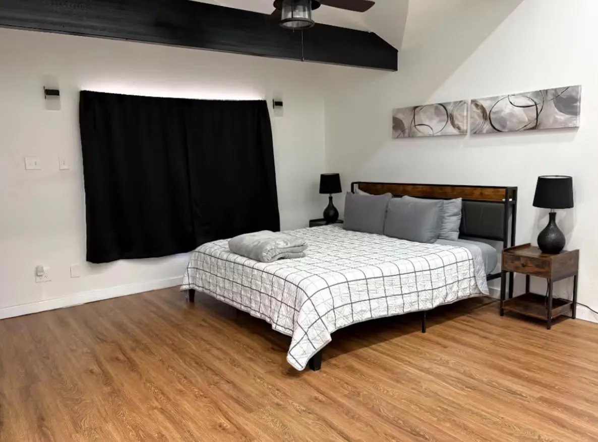 Spacious room featuring vaulted ceilings with exposed dark beams, wood-finish flooring, and white walls