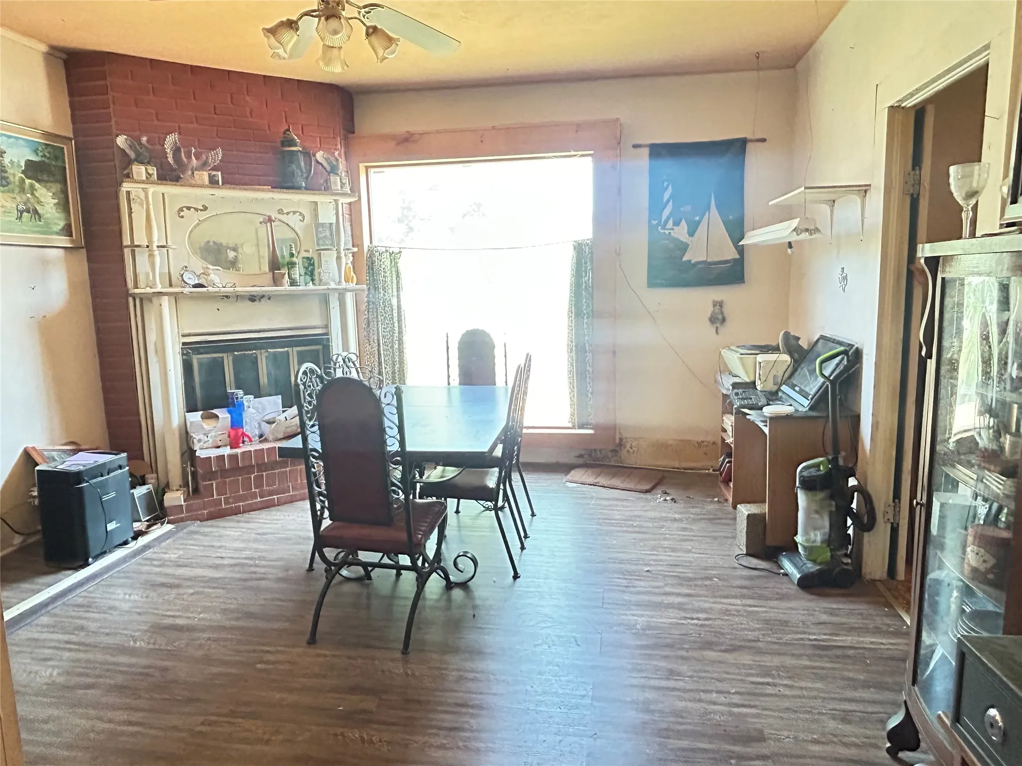 Dining room features luxury vinyl flooring, a large picture window, and a classic brick fireplace with a decorative mantle.