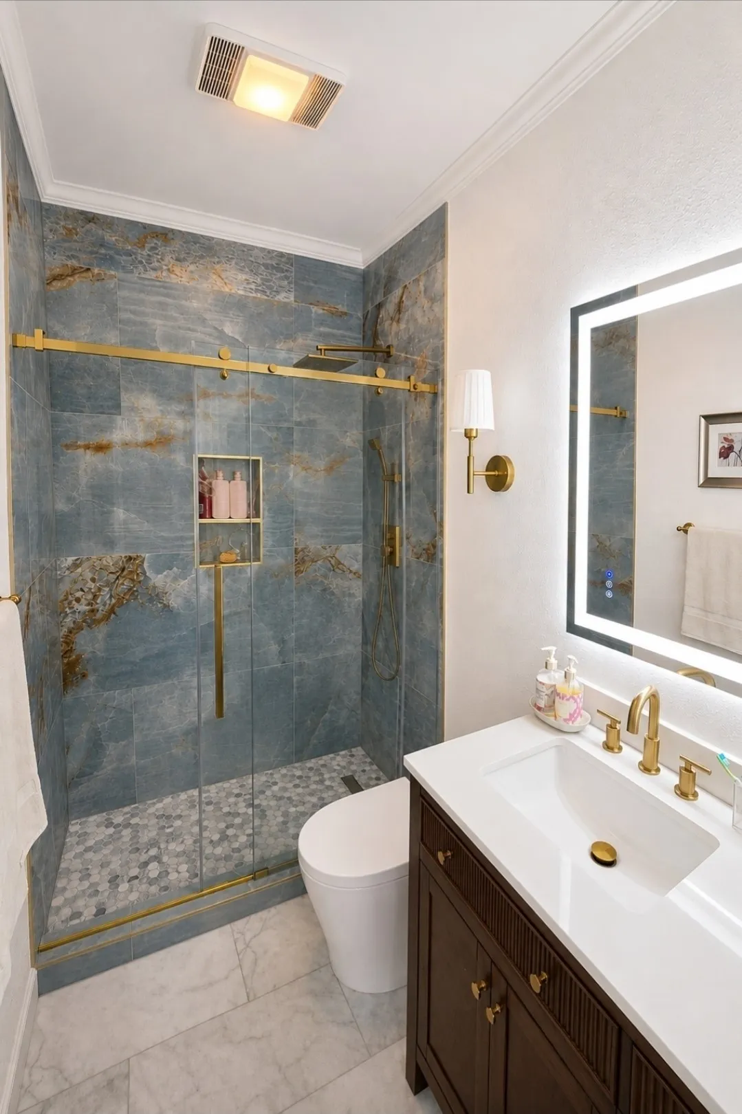 Modern bathroom featuring a glass-enclosed shower with blue-toned tile, a built-in shower niche, and a pebble tile floor