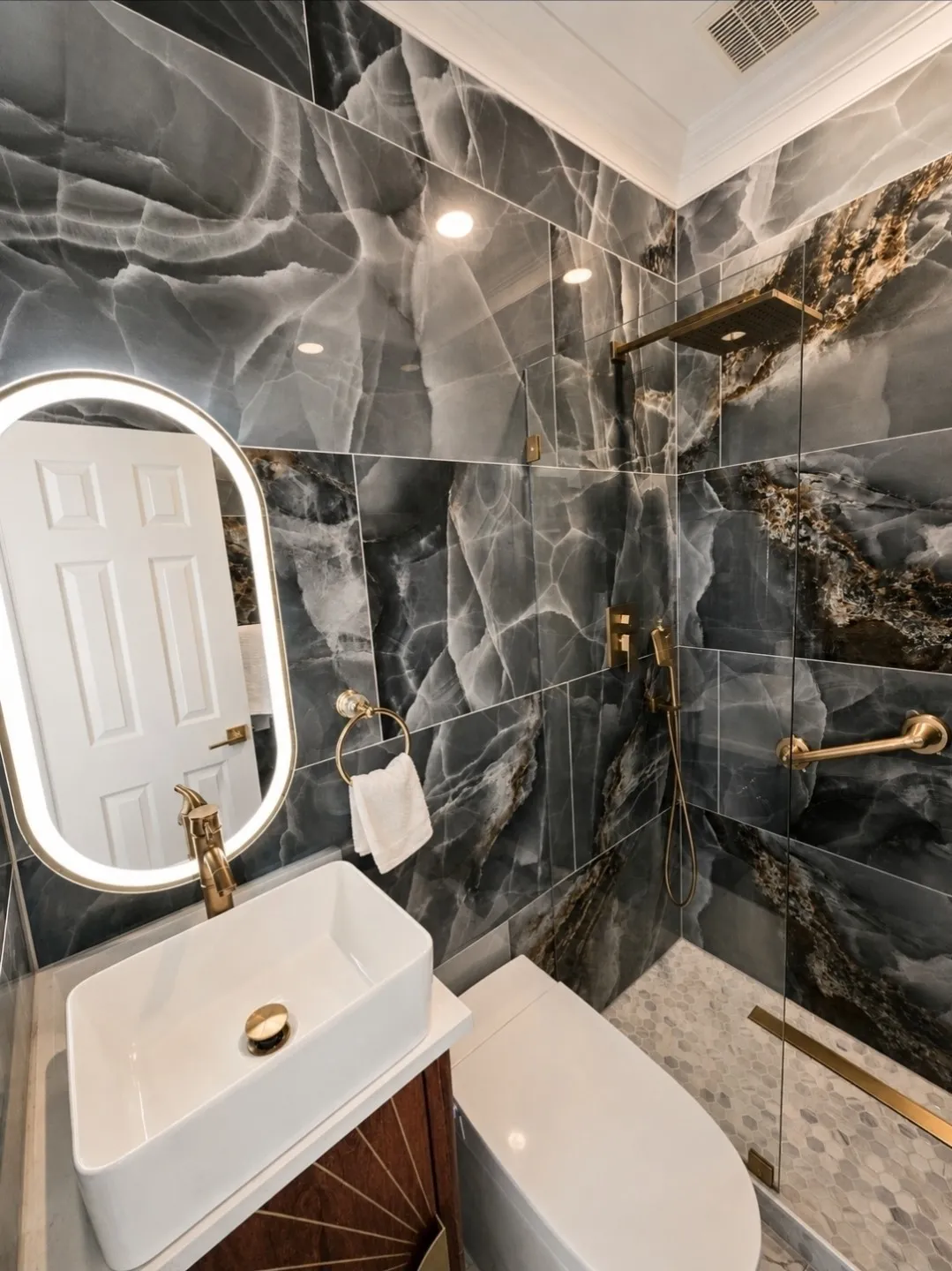 Luxurious bath featuring full-height stone-look tile walls, a contemporary vessel sink with a gold-tone faucet, and a frameless glass shower enclosure