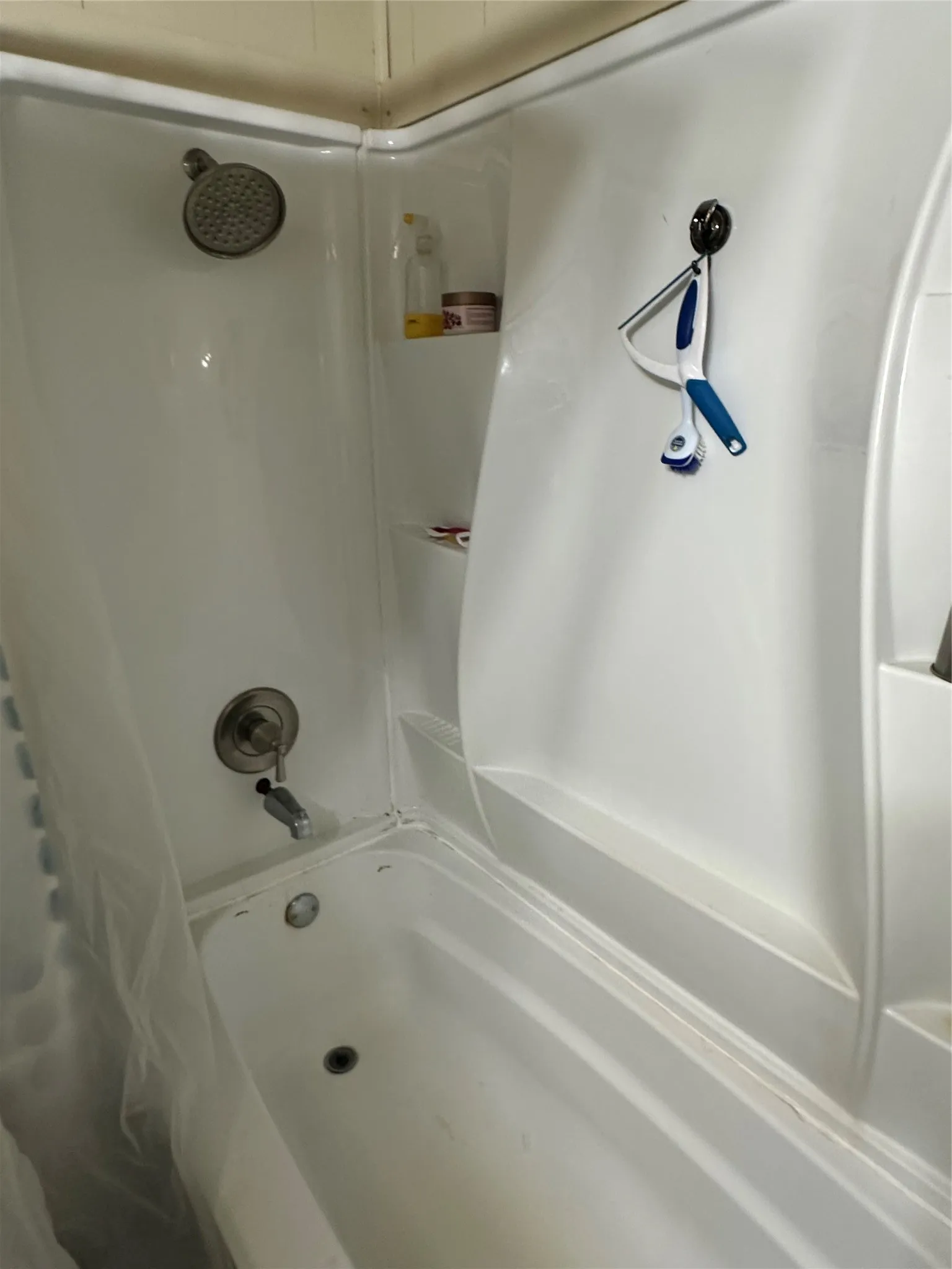 White bathtub and shower combination unit featuring a built-in shelf and integrated showerhead