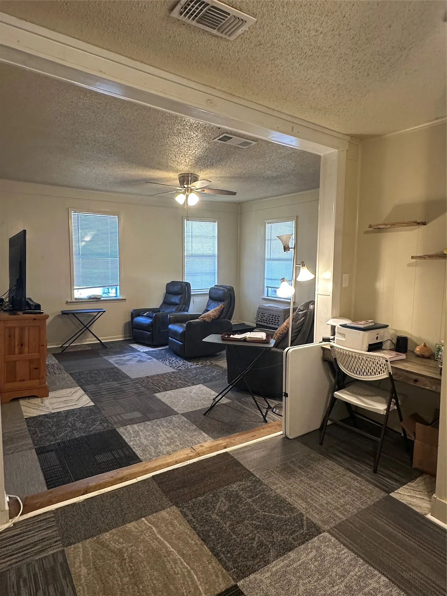 Open-concept area featuring multi-toned carpet squares, white trim, and a ceiling fan with integrated lighting