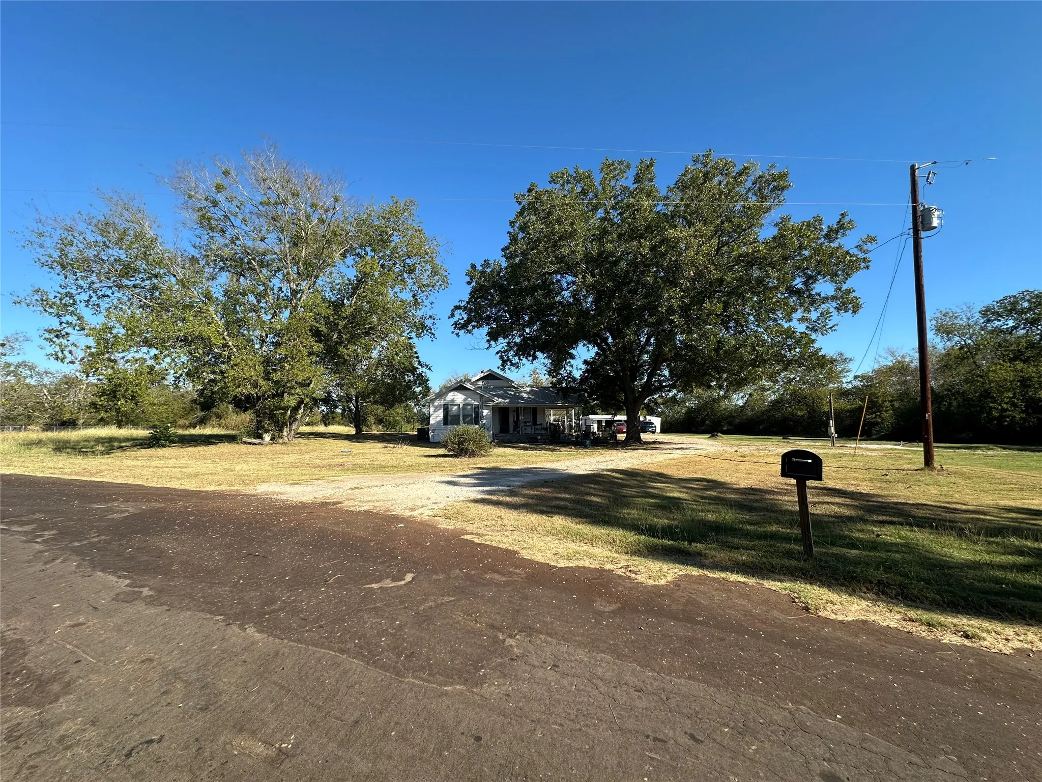 Front exterior featuring a white-sided residence with a covered porch and mature trees