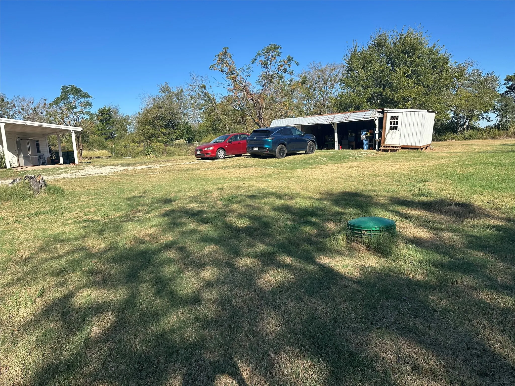 Expansive grassy yard with a detached covered carport and a separate utility shed