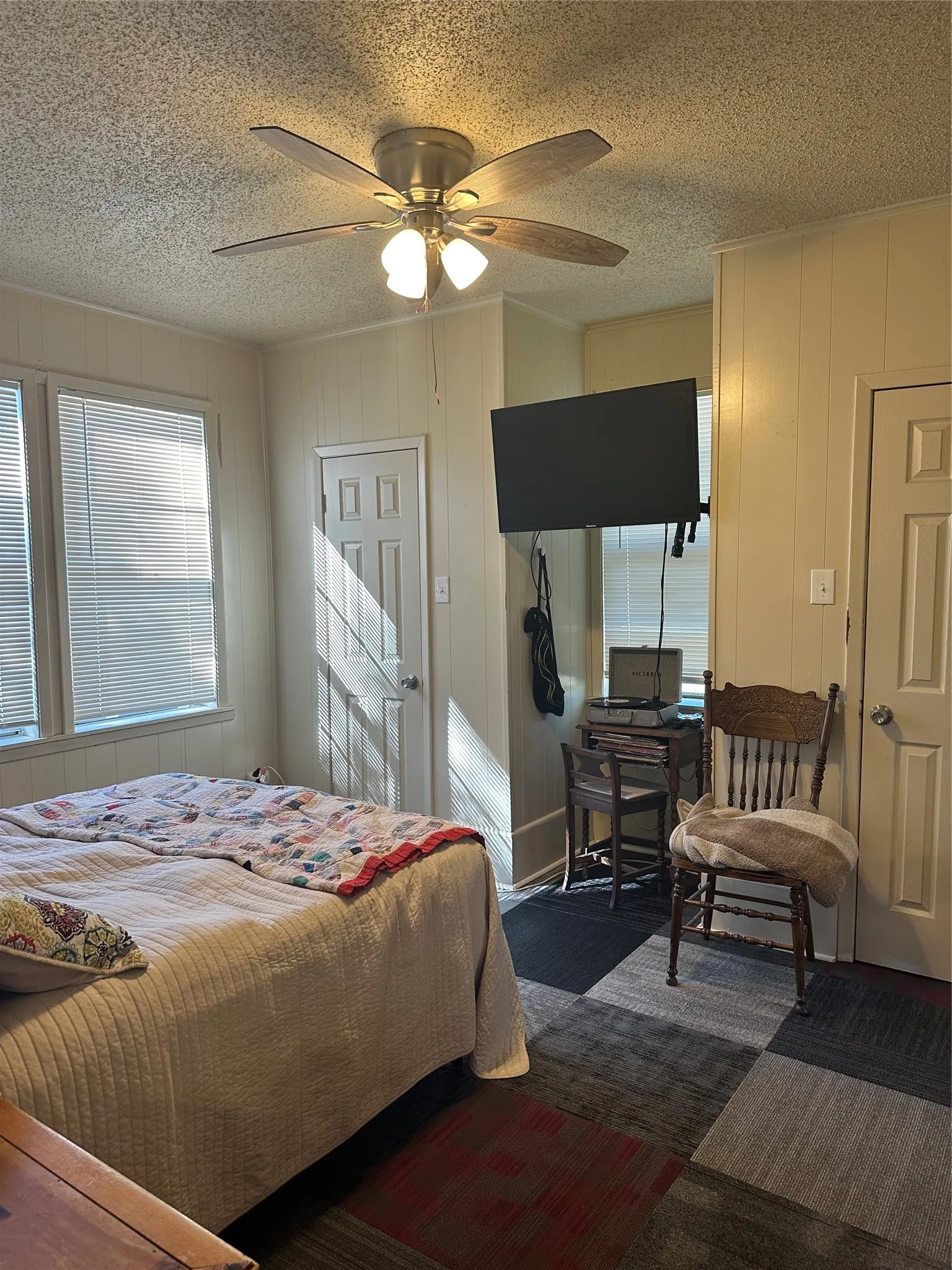 Bedroom featuring paneling walls, a ceiling fan with integrated lighting, and multiple windows with blinds
