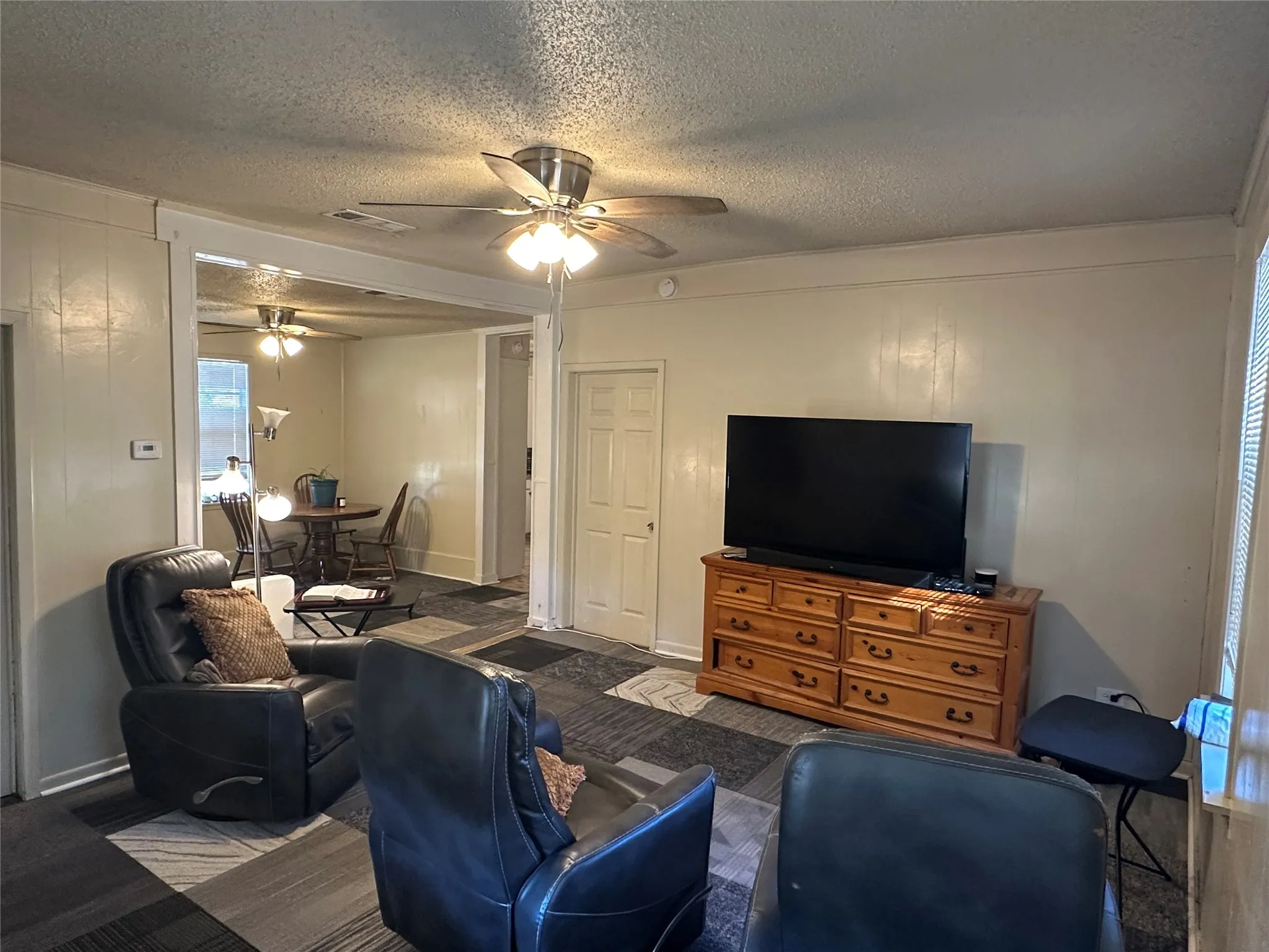 Living area featuring a ceiling fan, light-toned wall paneling, and a distinct floor pattern
