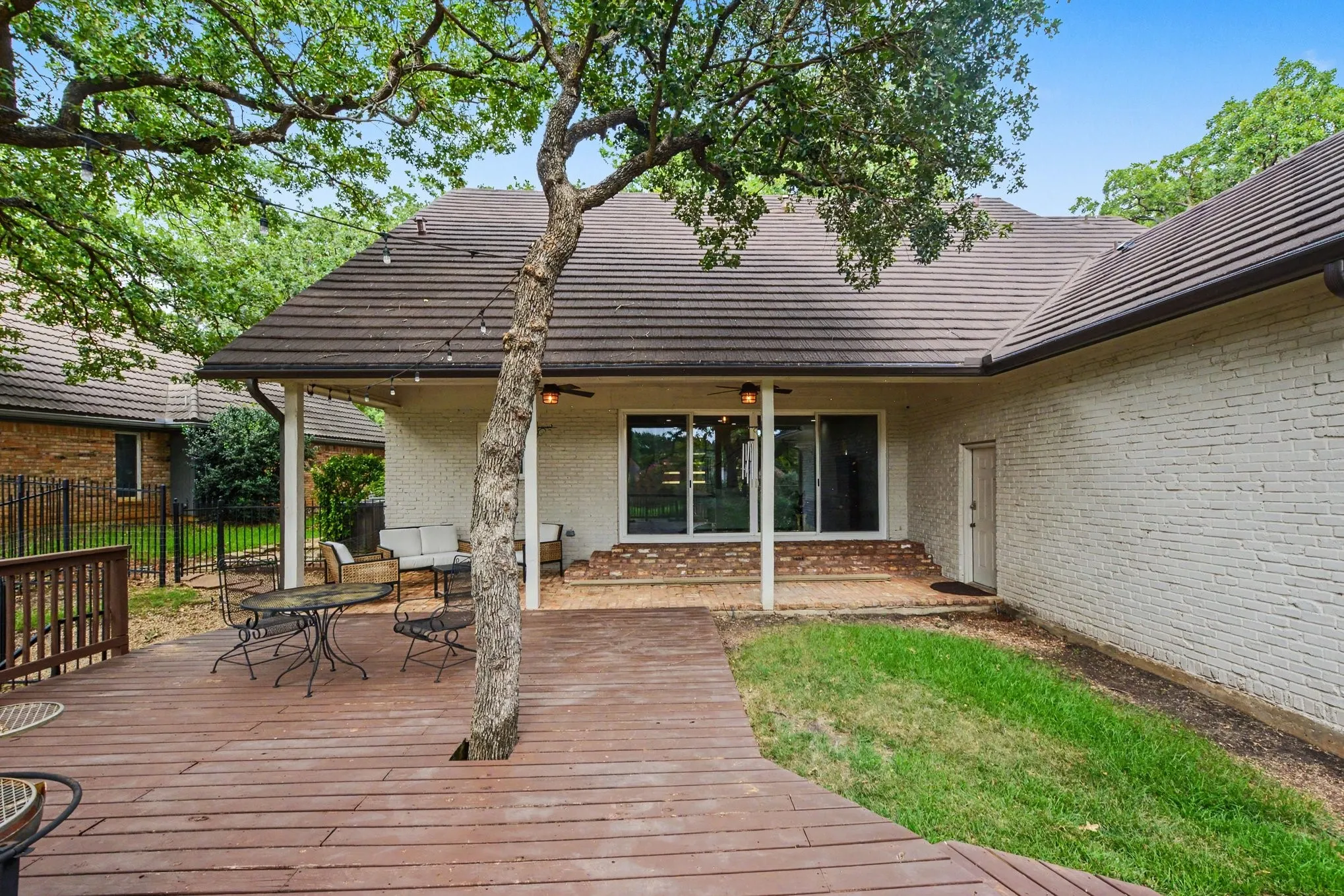 Spacious outdoor deck with mature tree integration, leading to a covered patio featuring a full-width sliding glass door