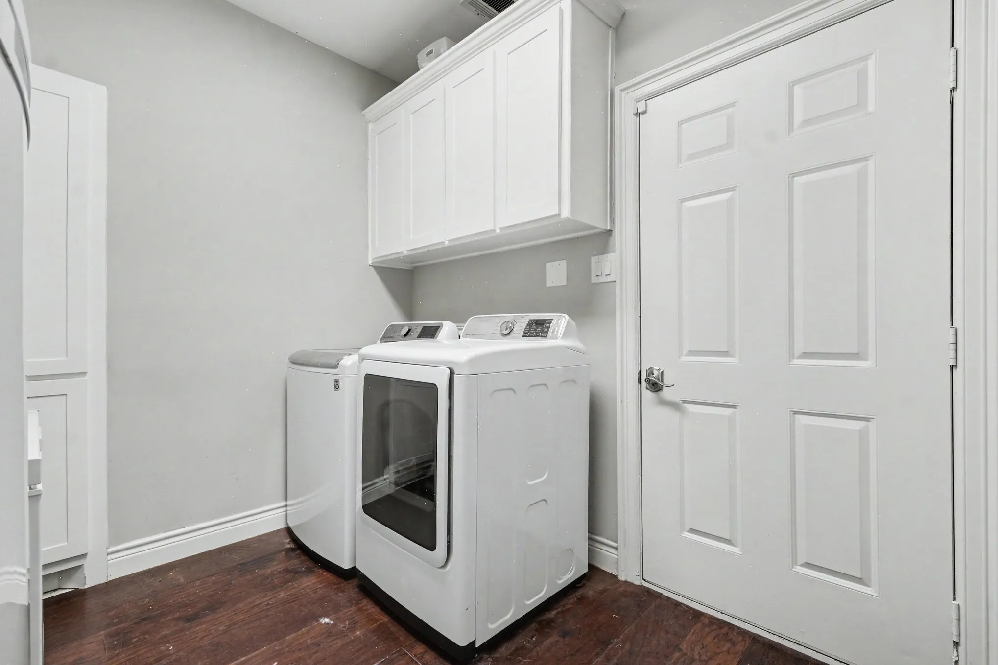 Laundry area featuring overhead cabinetry, a tall storage cabinet, wood-finish flooring, and light gray walls