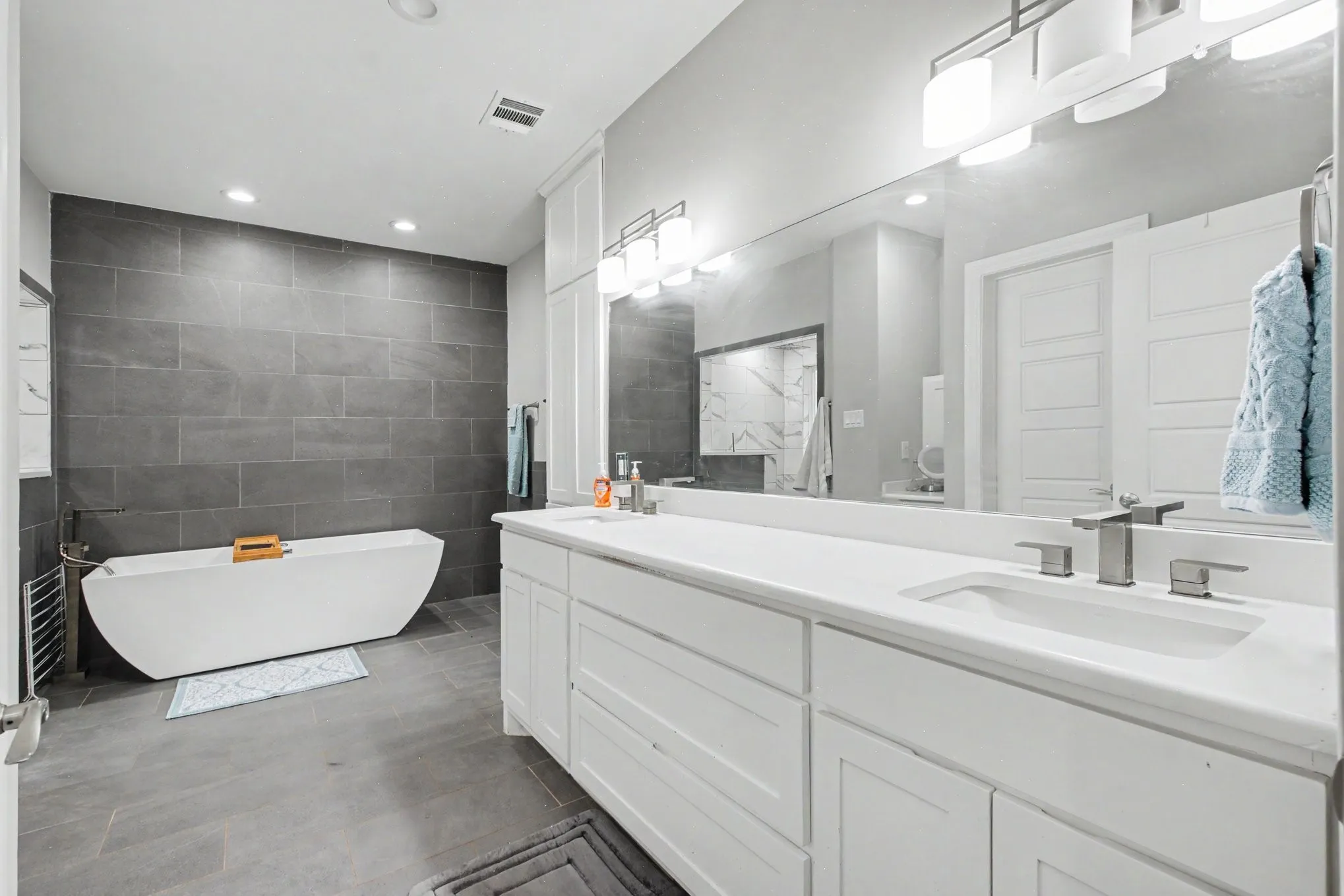 Contemporary bathroom featuring a freestanding soaking tub, a large vanity with dual sinks, and white shaker cabinetry