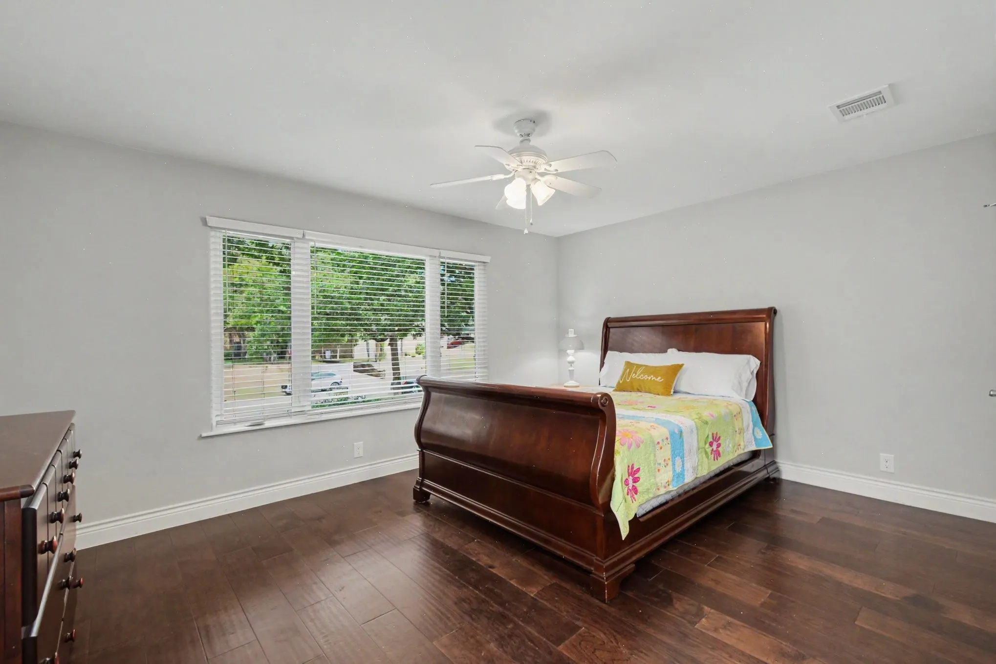 Spacious room featuring wood-finish flooring, a multi-pane window with white blinds, and a ceiling fan with integrated lighting