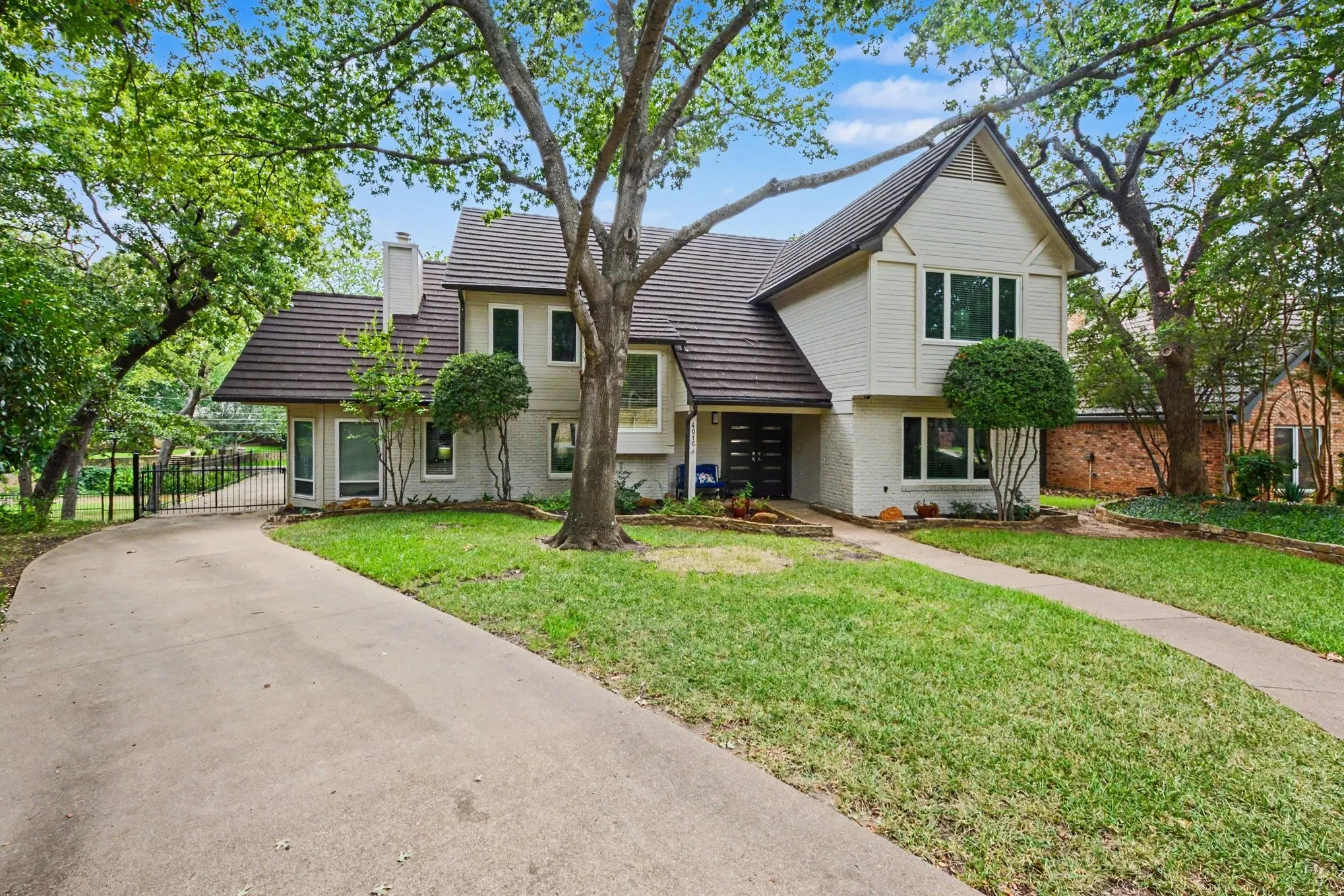 Two-story residence featuring a concrete driveway, a prominent tree, and a gated side entrance