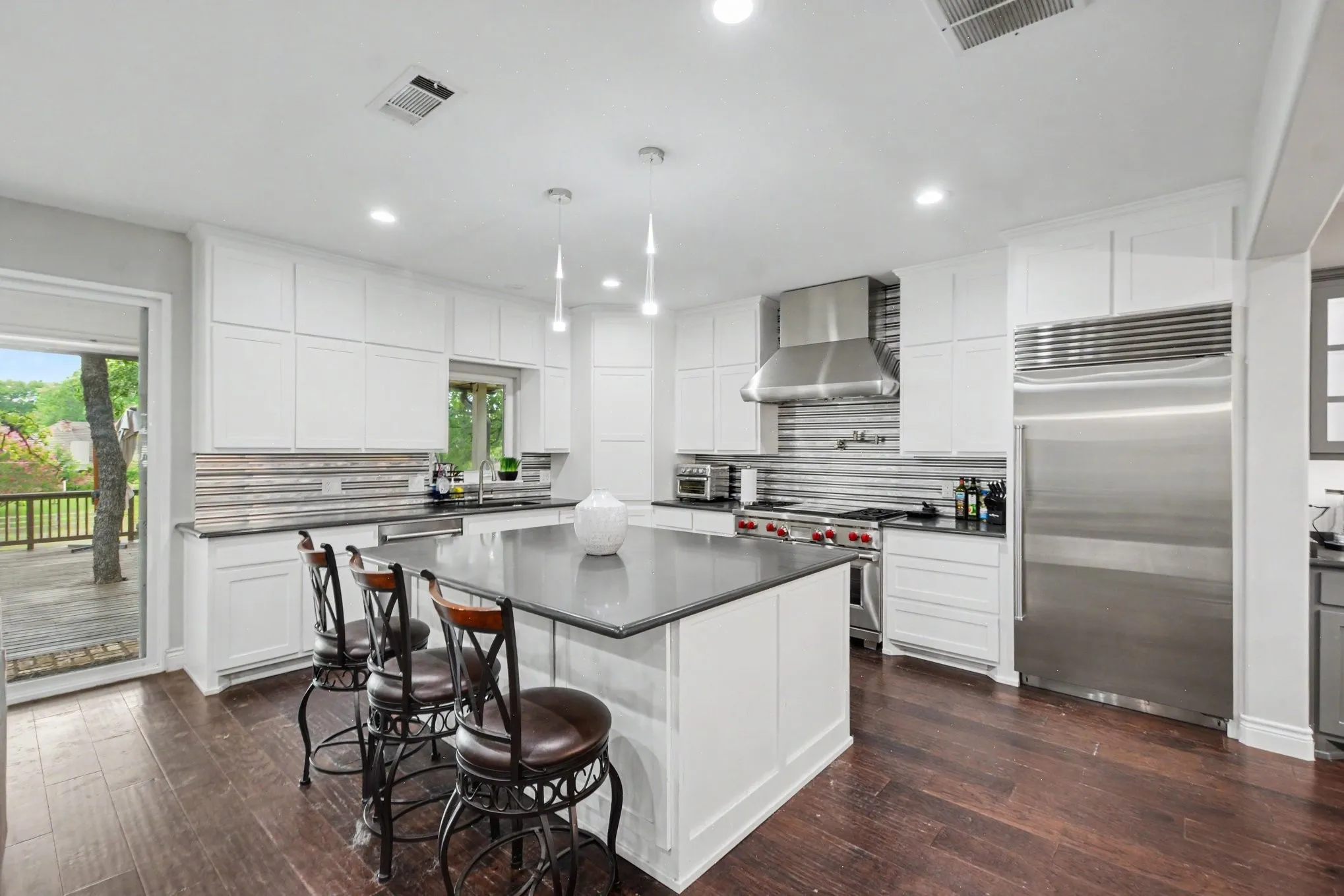 Modern kitchen featuring a large central island, white cabinetry, dark countertops, and stainless steel appliances