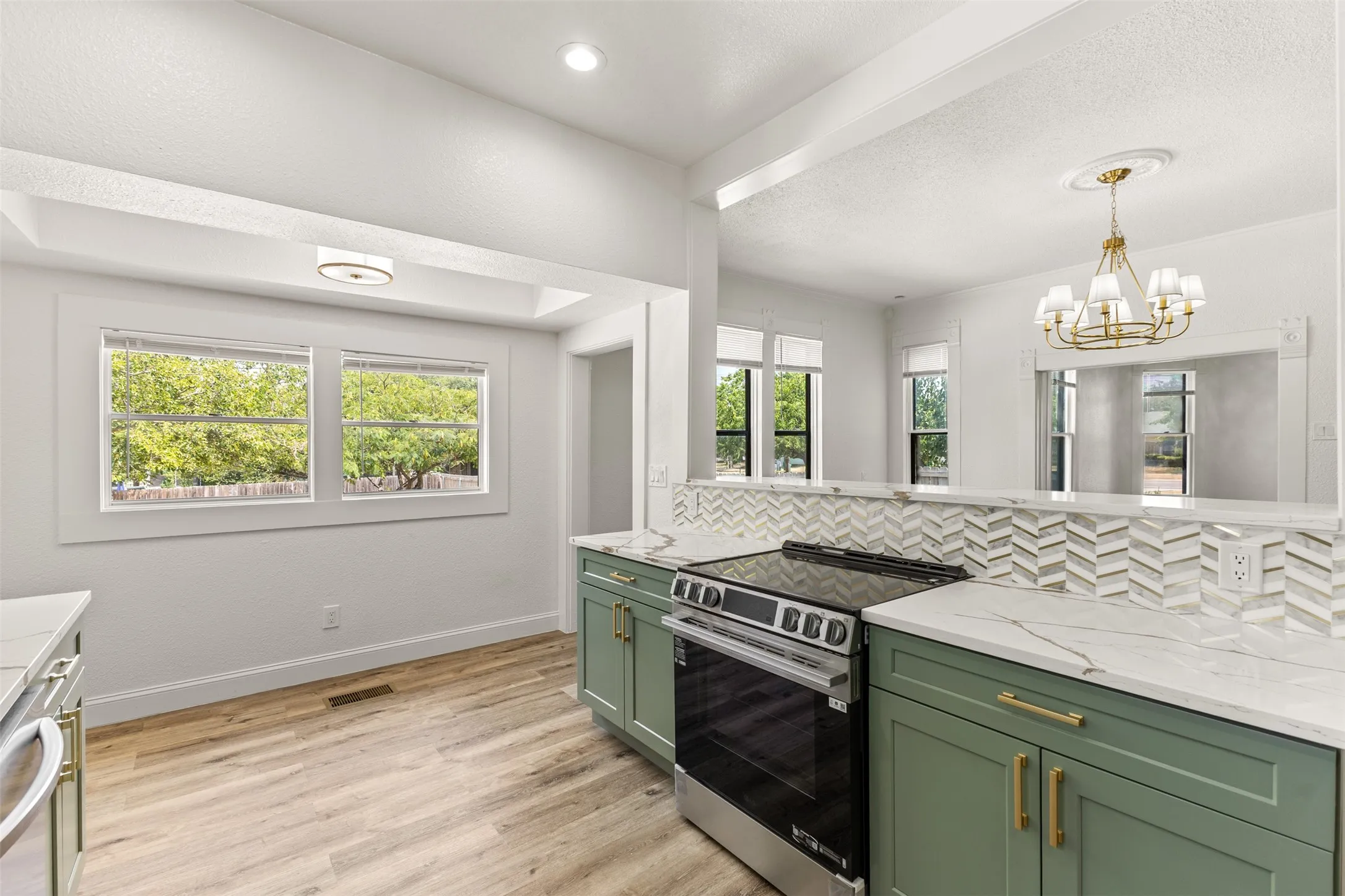 Modern kitchen featuring wood-finish flooring, light green cabinetry, white countertops, stainless steel range, and a herringbone tile backsplash
