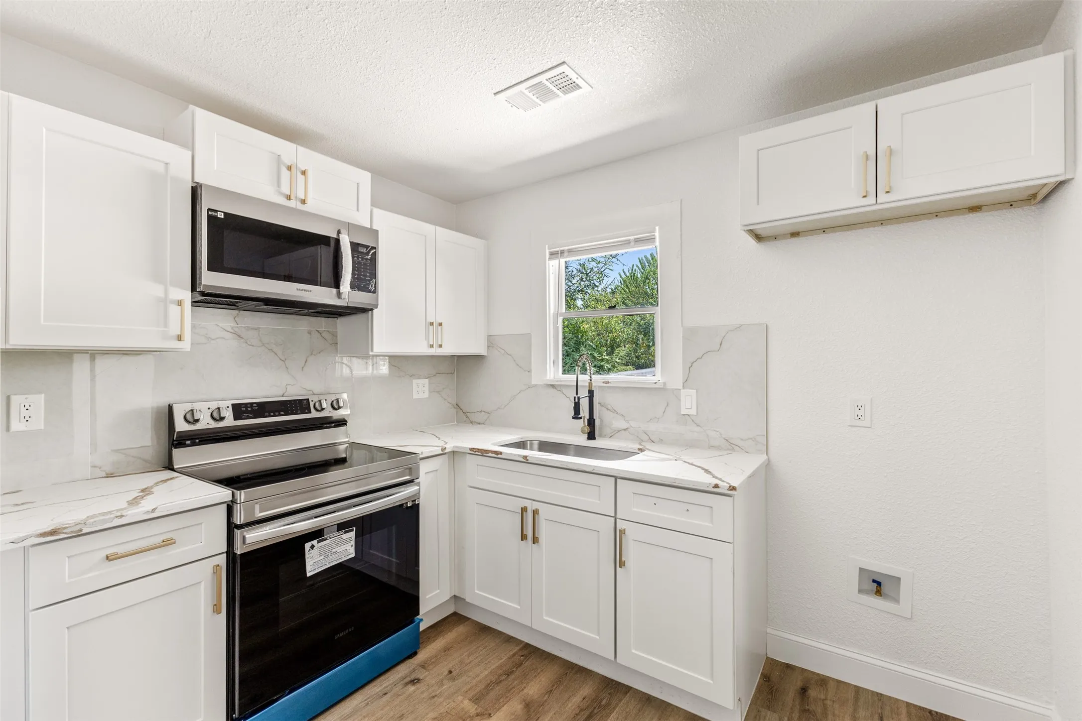 White cabinetry with gold-tone hardware, stainless steel appliances, and wood-finish flooring