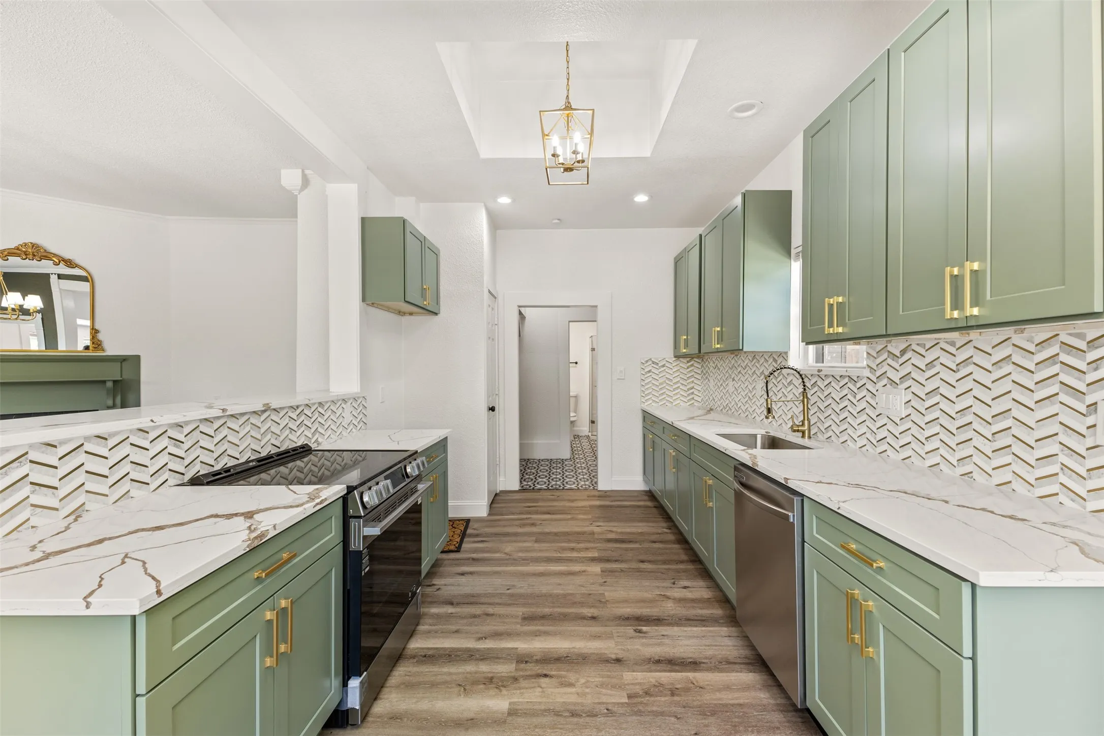 Galley kitchen featuring sage green cabinetry, white countertops with brown veining, herringbone tile backsplash, and stainless steel appliances