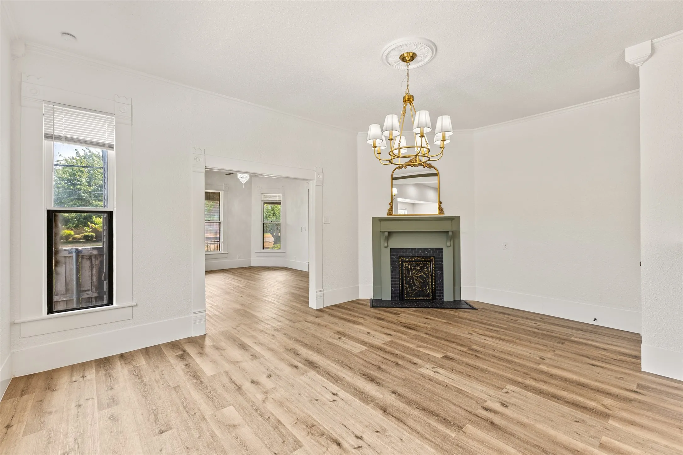 Wood-finish flooring throughout, featuring a decorative fireplace with a mantel, a brass chandelier, and white crown​​‌​​​​‌​​‌‌​‌‌​​​‌‌​‌​‌​‌​​​‌​​ molding