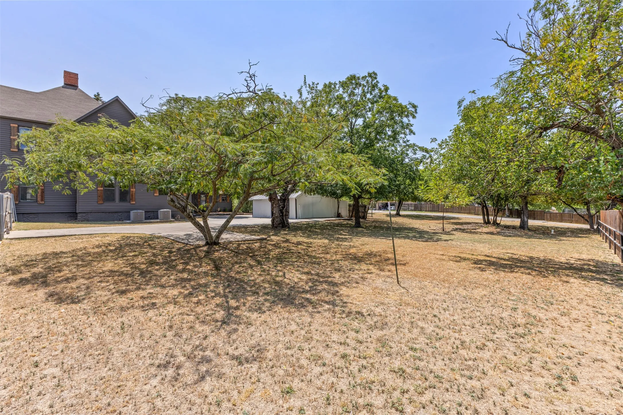 Expansive yard with mature trees, a wooden fence, and a paved driveway