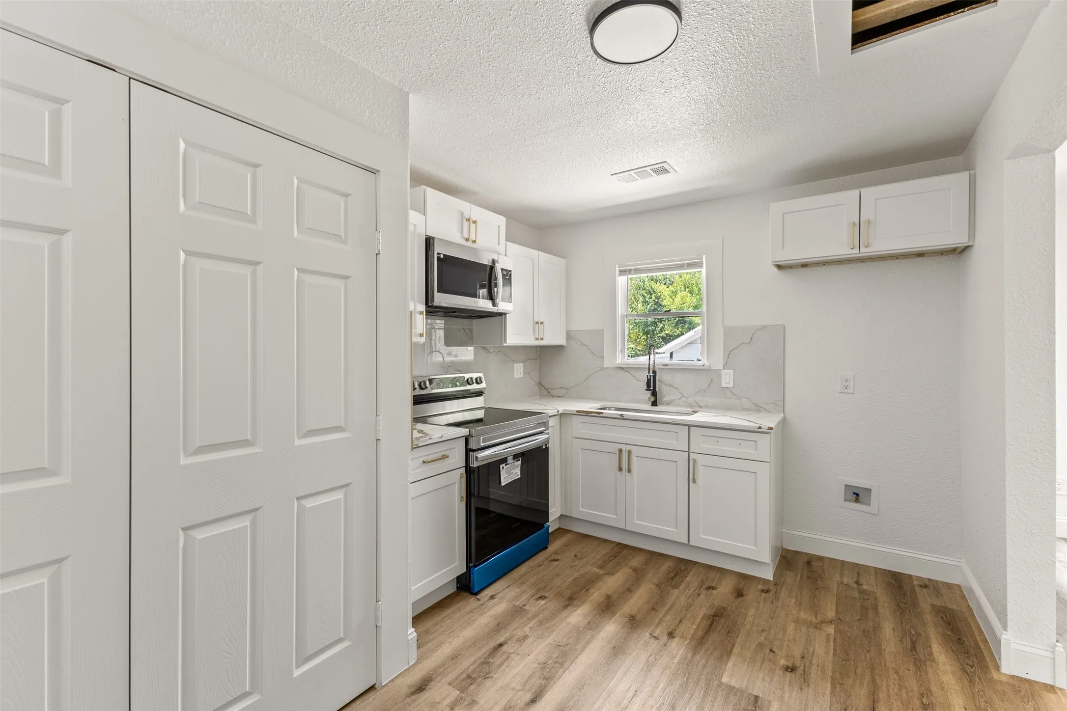 Kitchen featuring white cabinetry, light-toned wood-finish flooring, stainless steel microwave, and an electric range
