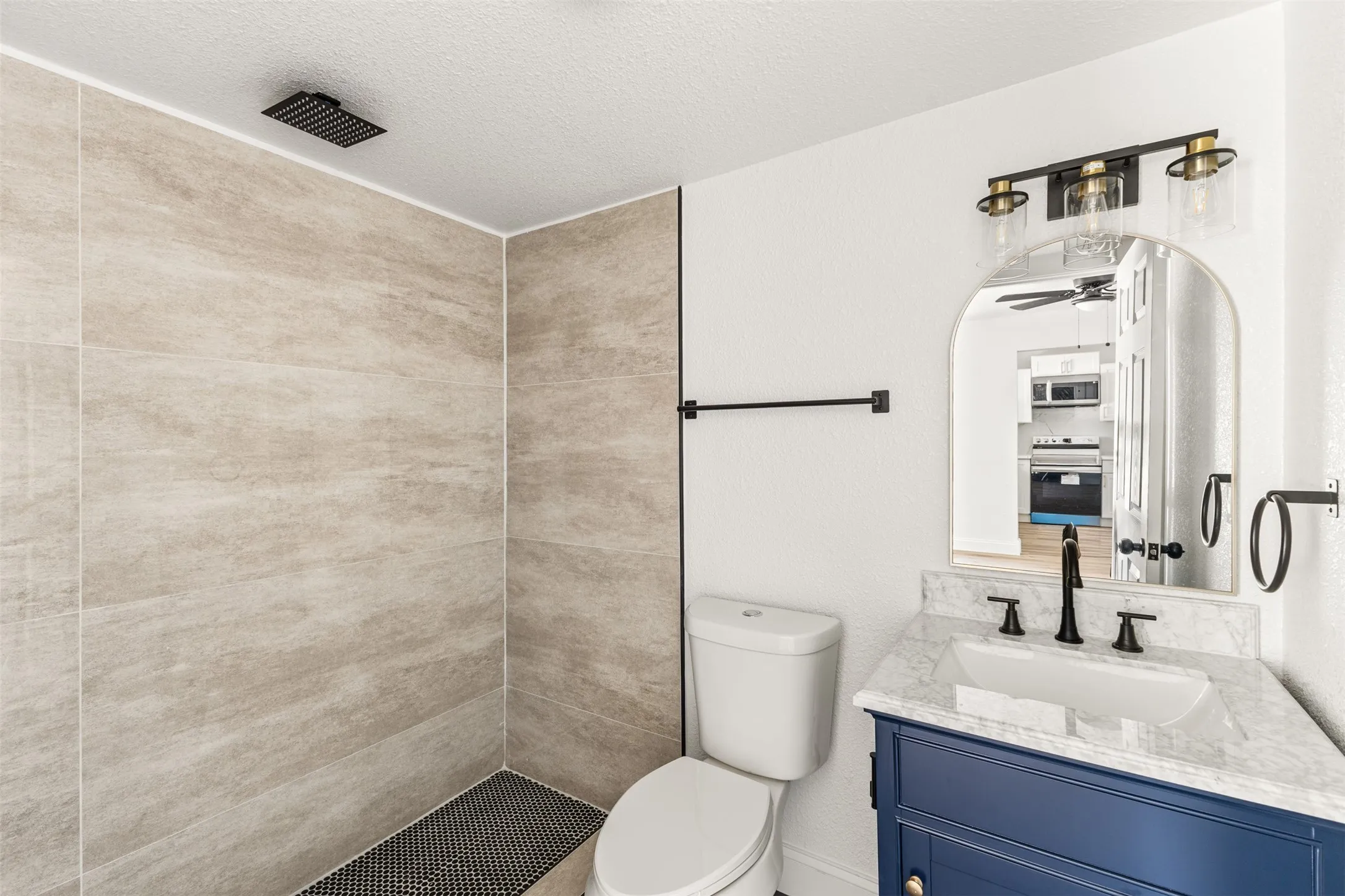 Walk-in shower with textured wall tiles and black penny tile flooring, featuring a black rainfall showerhead