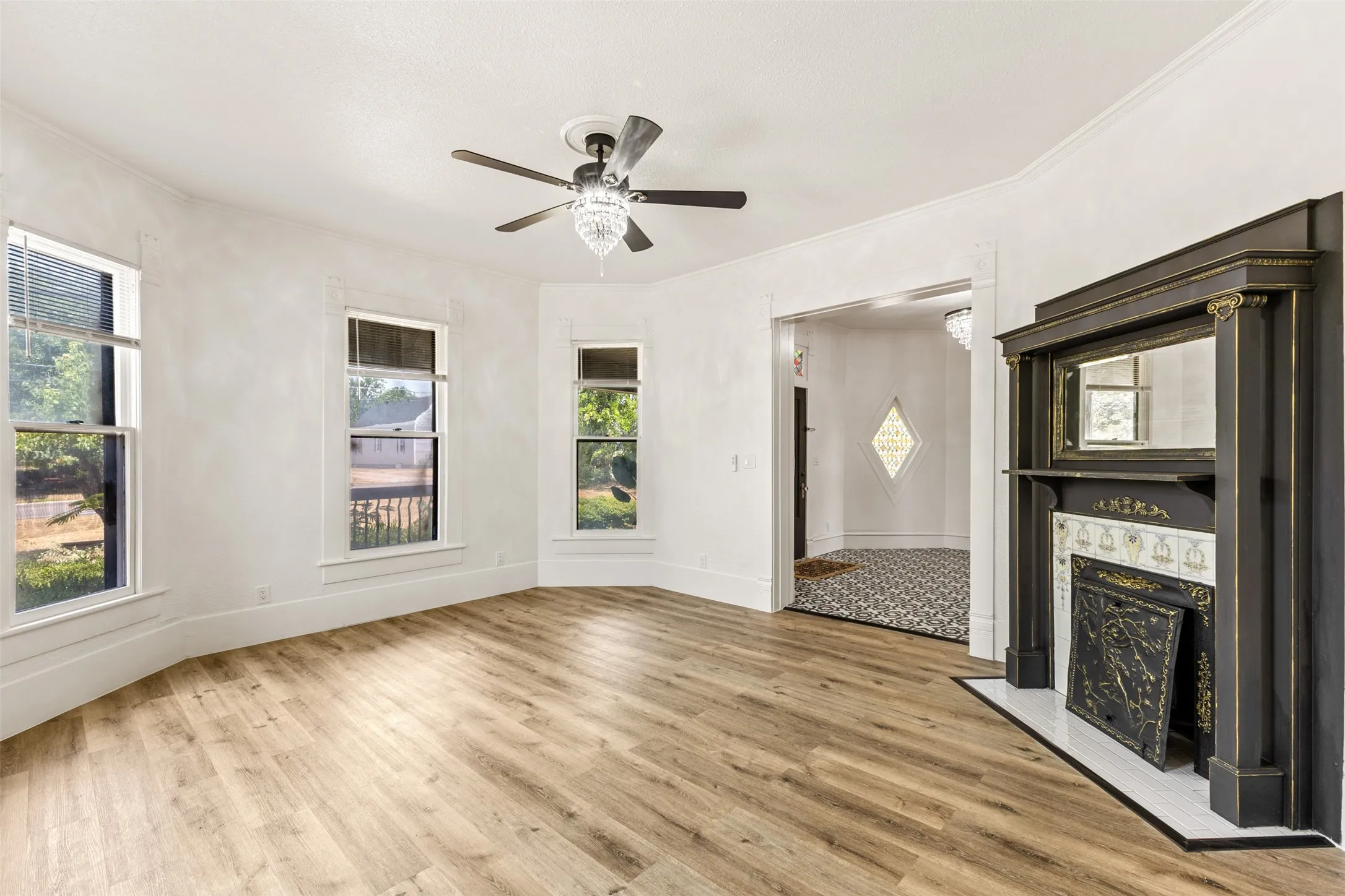 Bay window configuration, wood-finish flooring, decorative fireplace with tiled hearth, ceiling fan with crystal light fixture, and wide entryways