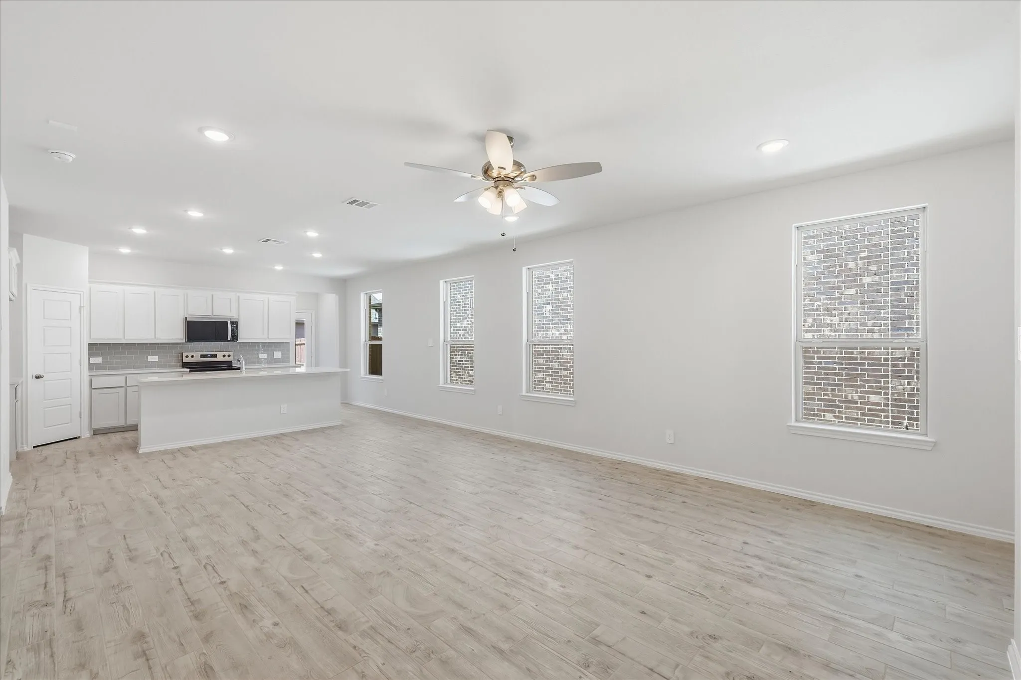Spacious open-concept living area featuring light wood-finish flooring and multiple windows