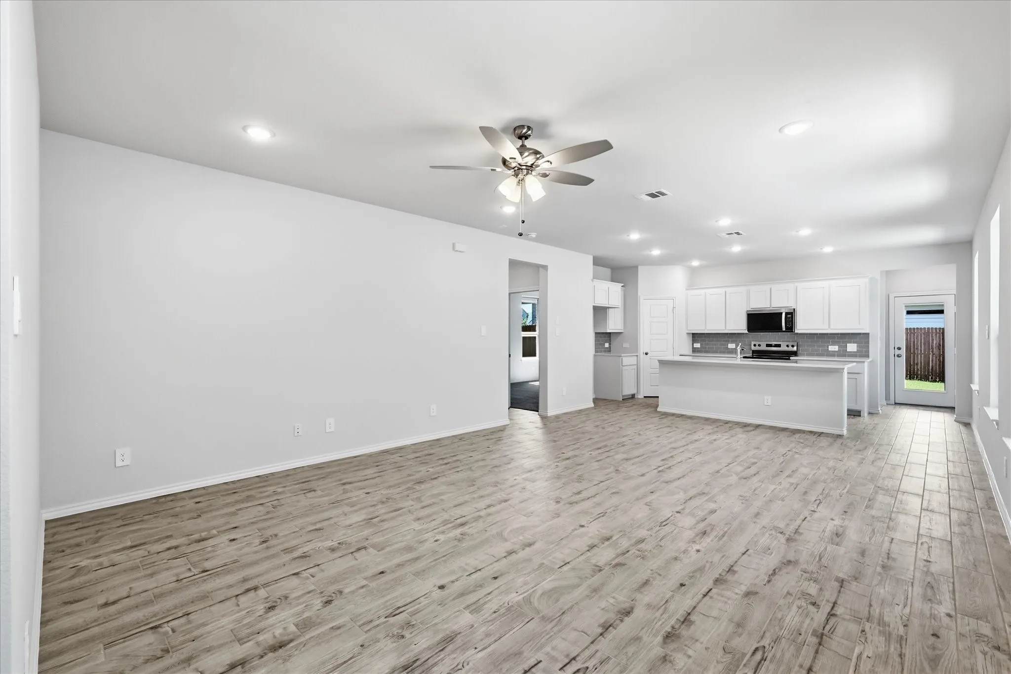 Expansive living area with wood-finish tile flooring, recessed lighting, and a ceiling fan