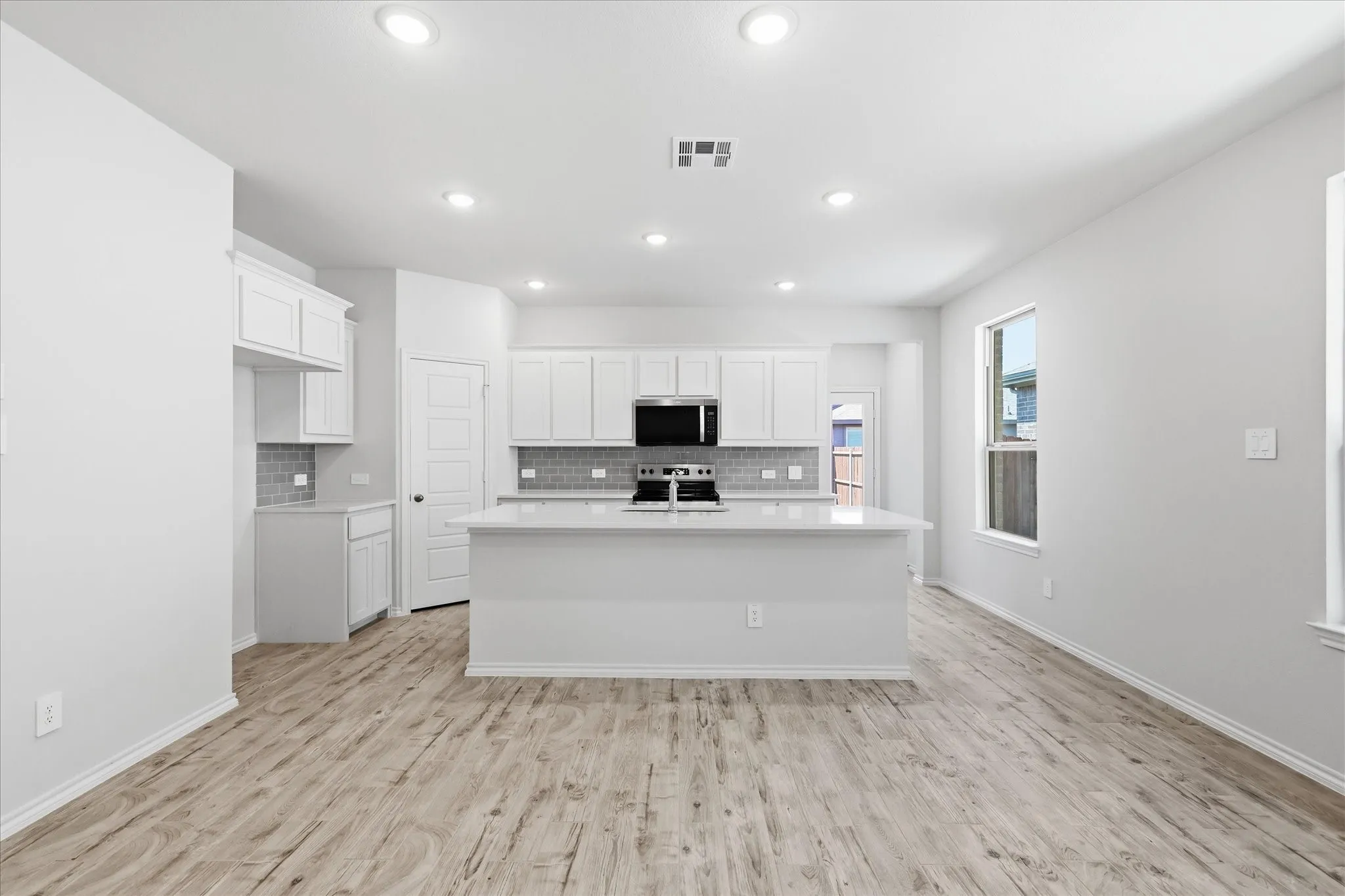 Open-concept kitchen featuring an island with a light-colored countertop, recessed lighting, wood-finish flooring, white cabinetry, and a tile backsplash