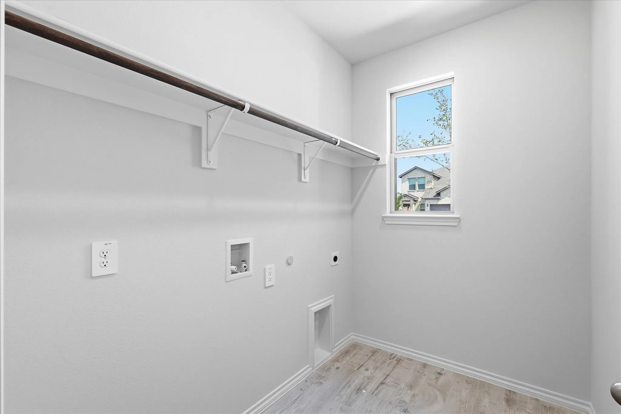 Dedicated utility area featuring wood-finish flooring, a bright window, and built-in shelving with a clothes rod