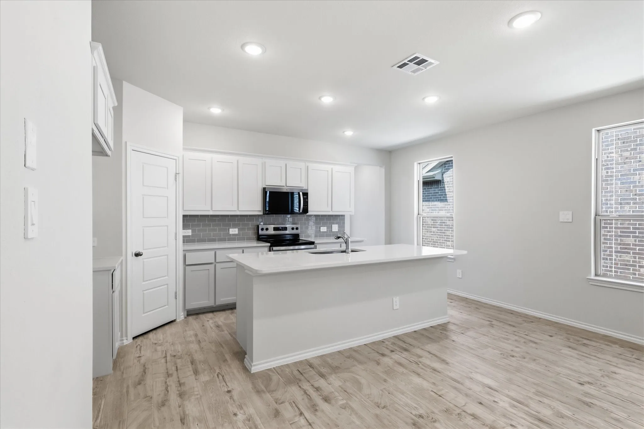 Modern kitchen featuring white cabinetry, a large center island with integrated sink, black appliances, a gray subway tile backsplash, and recessed lighting