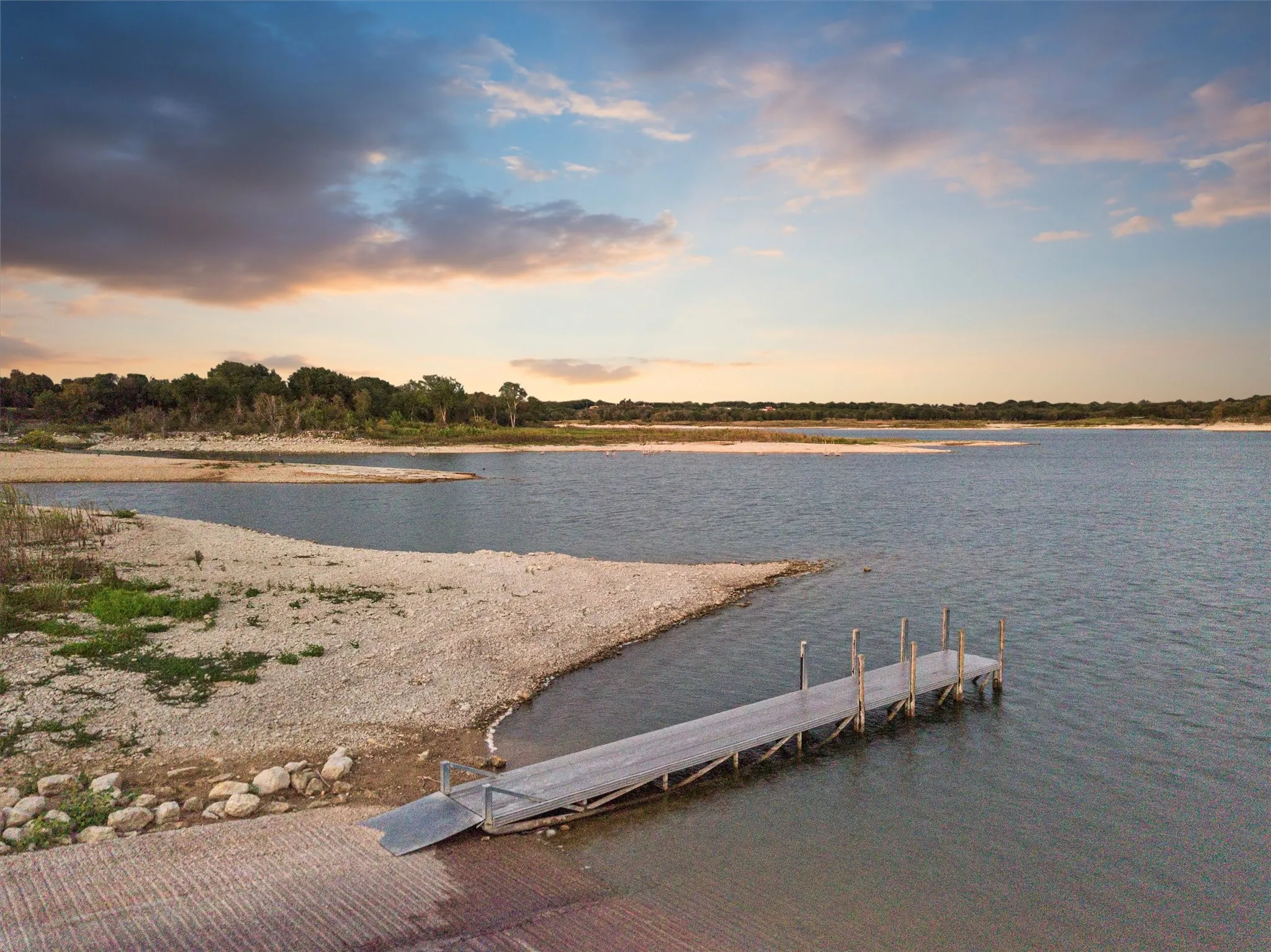 Private dock structure extending into the water, featuring a concrete boat ramp and a gravel shoreline