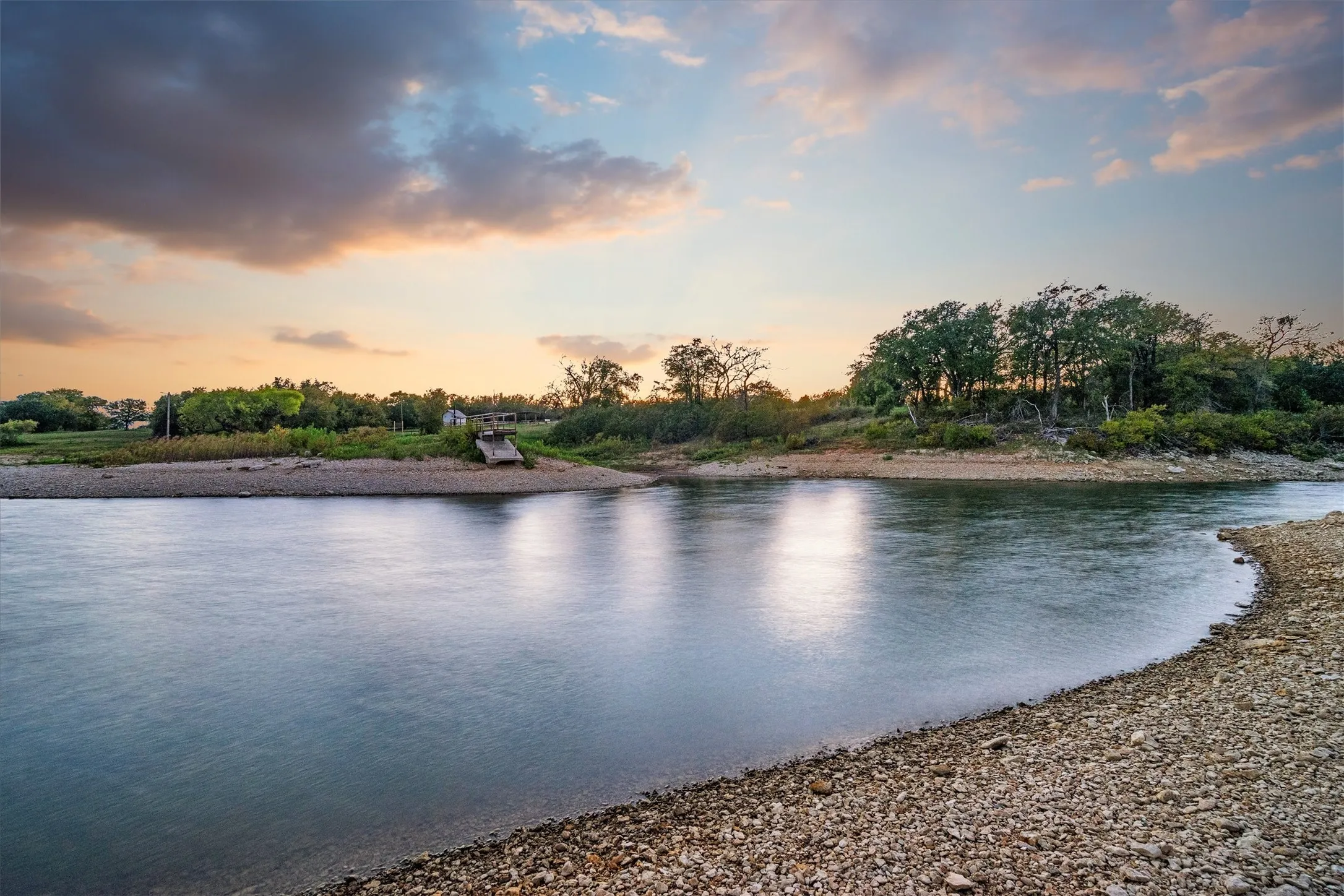 Riverfront property featuring a gravel shoreline and mature trees