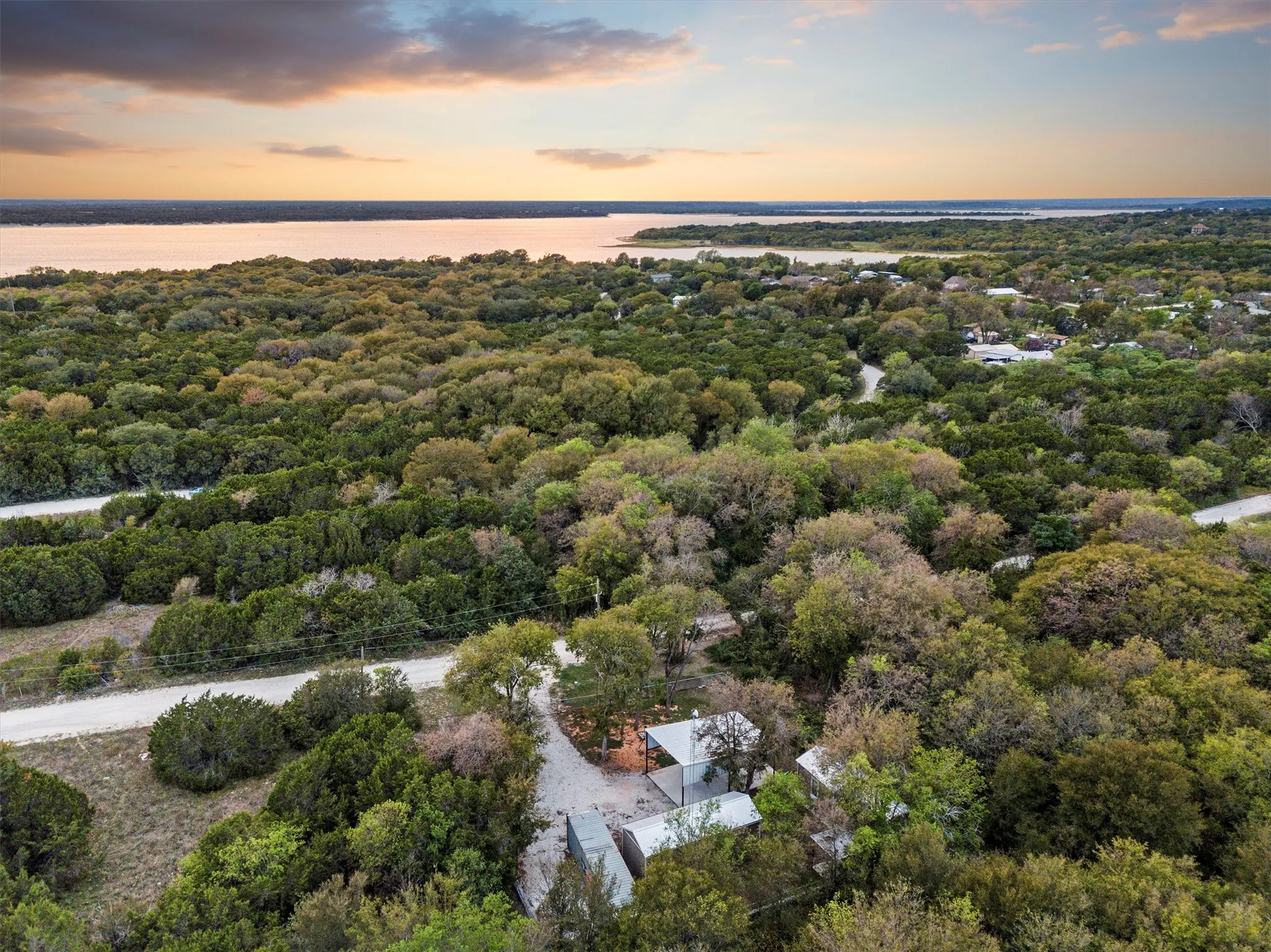 Aerial perspective showcasing a dense tree canopy surrounding a residence with a water body in the background