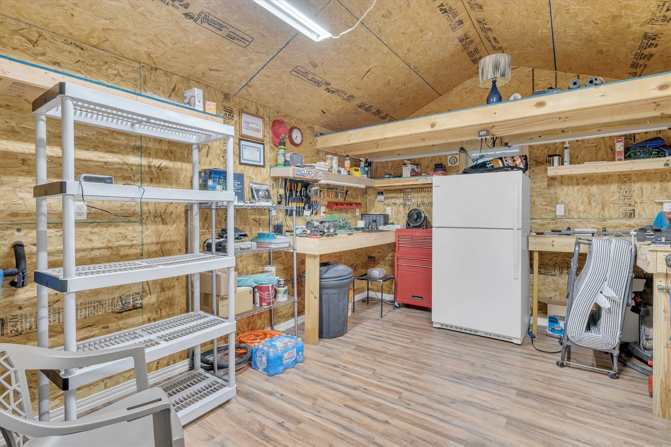 Versatile utility space featuring wood-finish flooring, exposed plywood walls, and overhead fluorescent lighting
