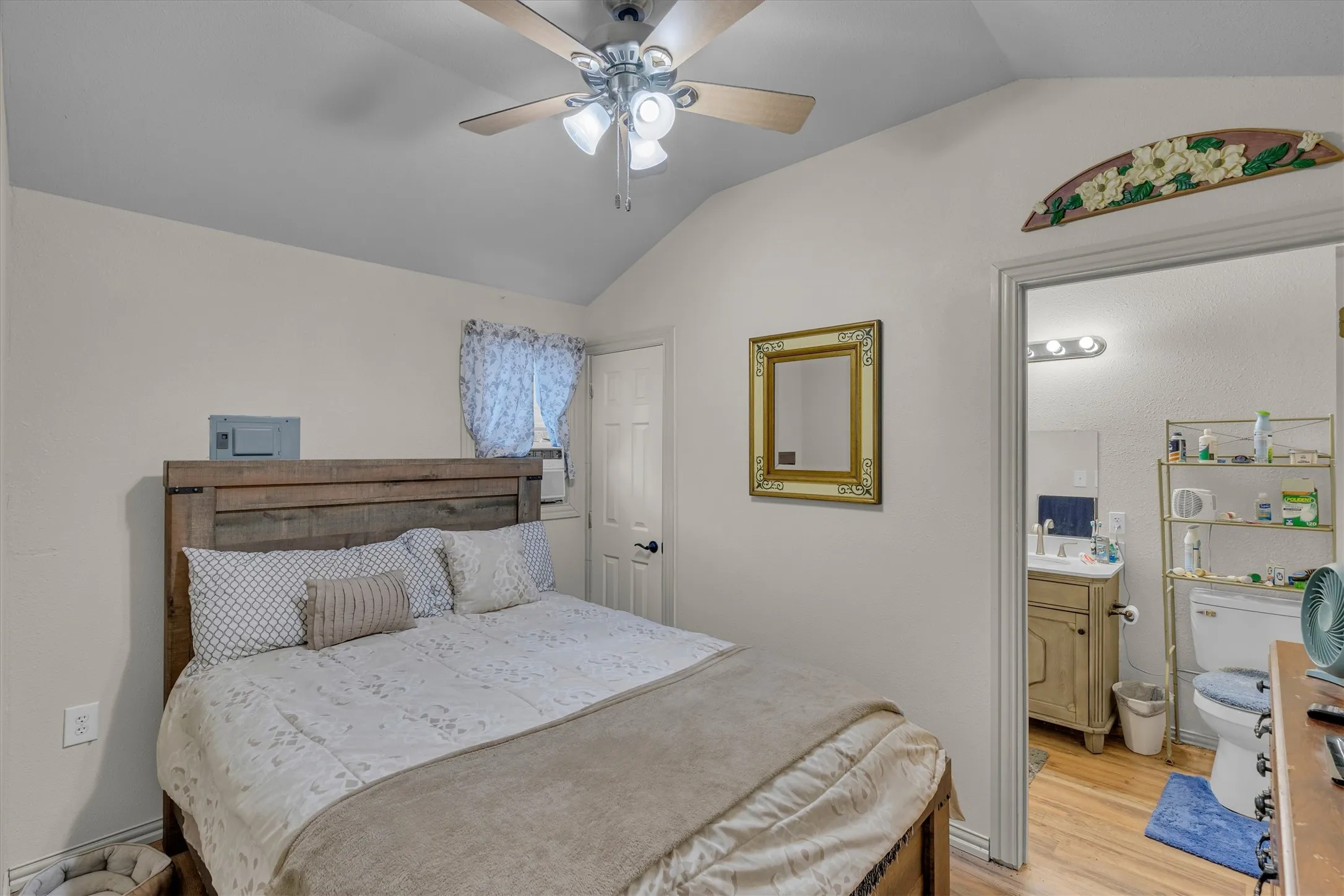Vaulted ceiling bedroom featuring a ceiling fan with light fixture and wood-finish flooring
