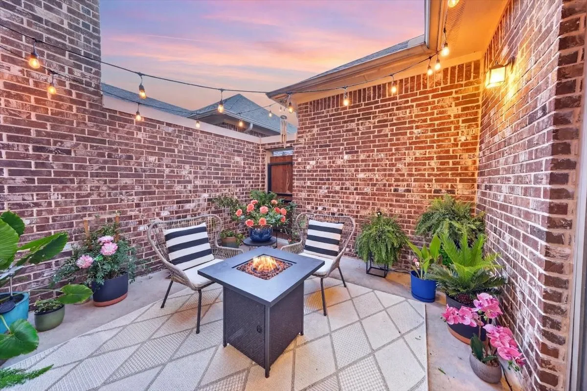 Brick-walled patio featuring string lighting, a built-in outdoor wall light, and a concrete surface