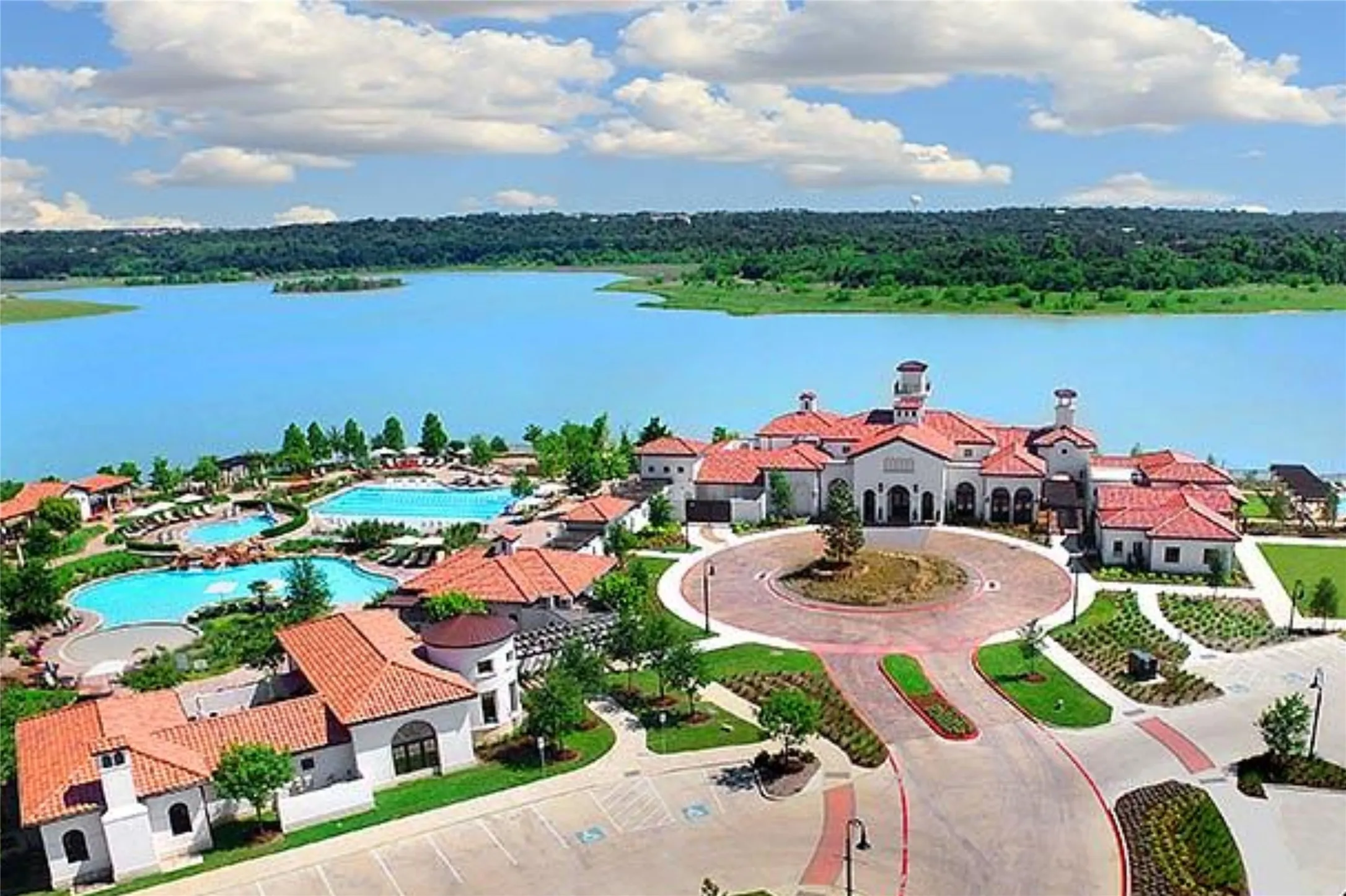 Expansive lakeside resort-style development featuring multiple swimming pools, a central clubhouse with a circular drive, terracotta-tiled roofs, and mature landscaping