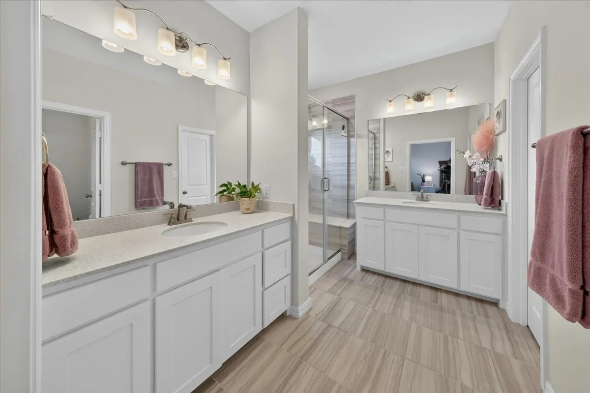 Dual vanity sinks with stone countertops, white cabinetry, a glass-enclosed shower with a built-in bench, and wood-look tile flooring
